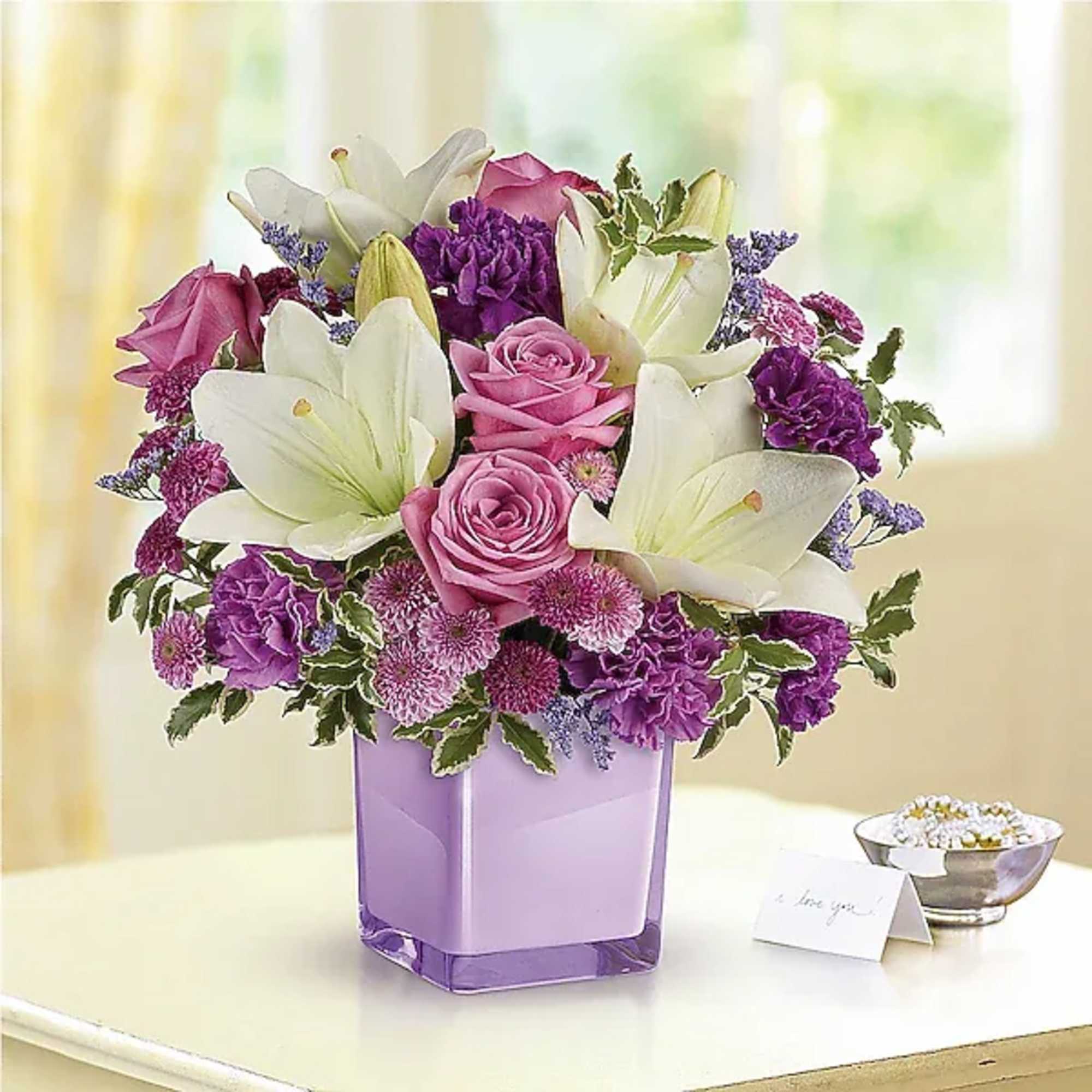 Pink and white flower arrangement in a purple glass vase
