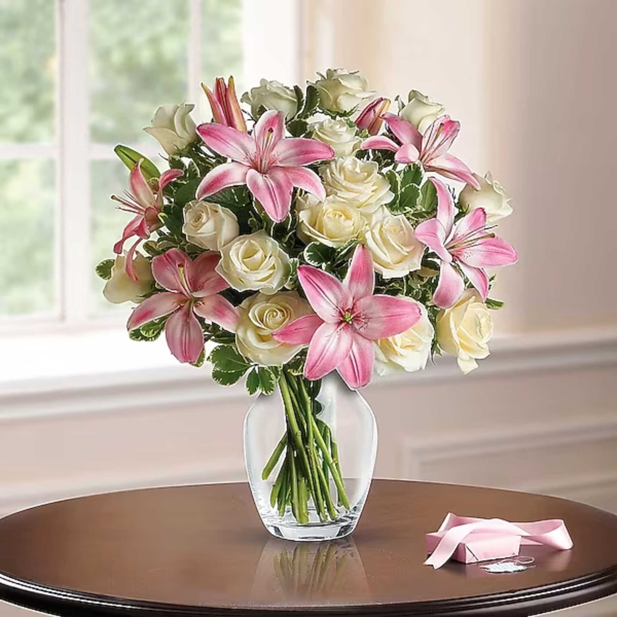 Pink lilies and white roses in a clear glass vase on a table