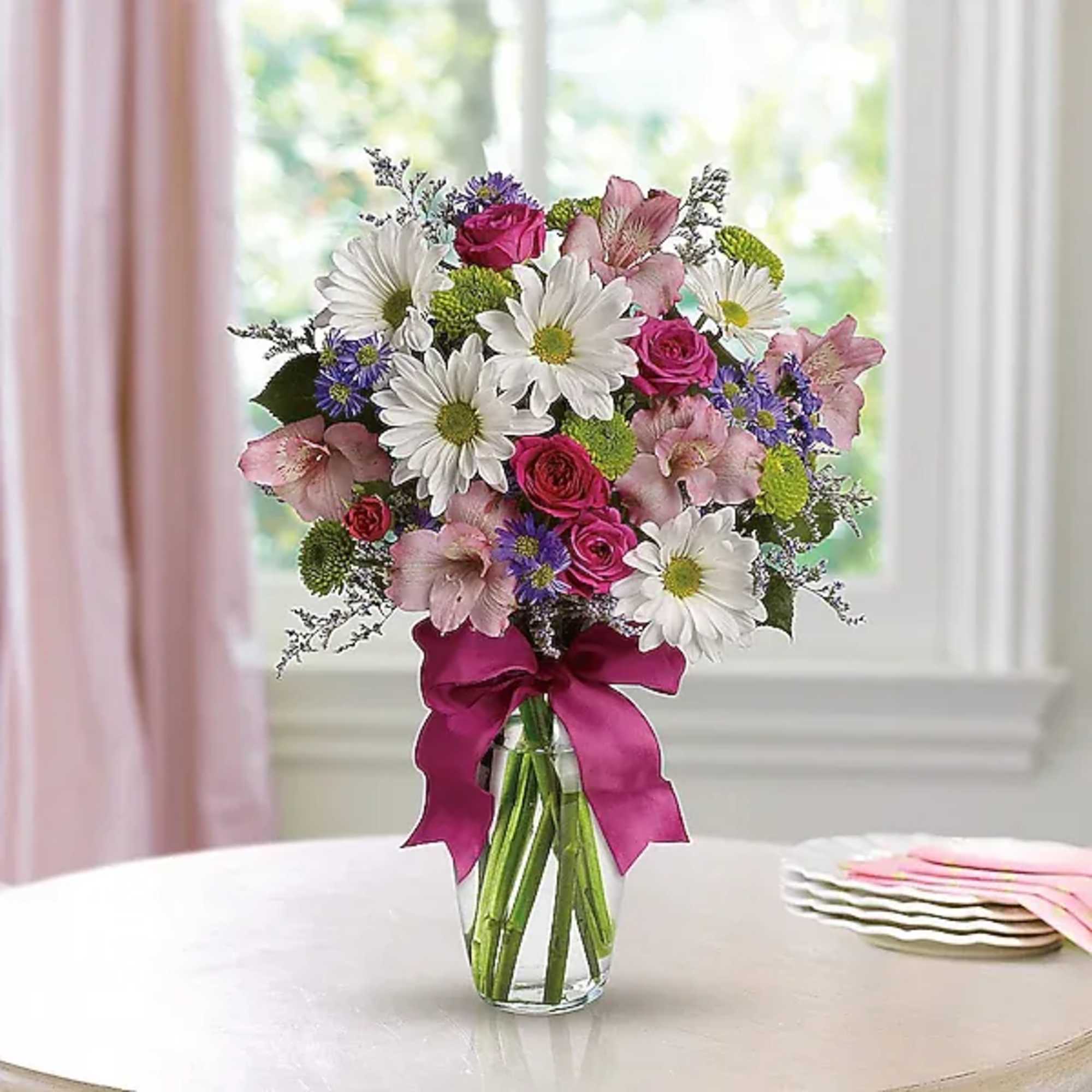 Bouquet of white daisies, pink roses, and purple flowers in a glass vase