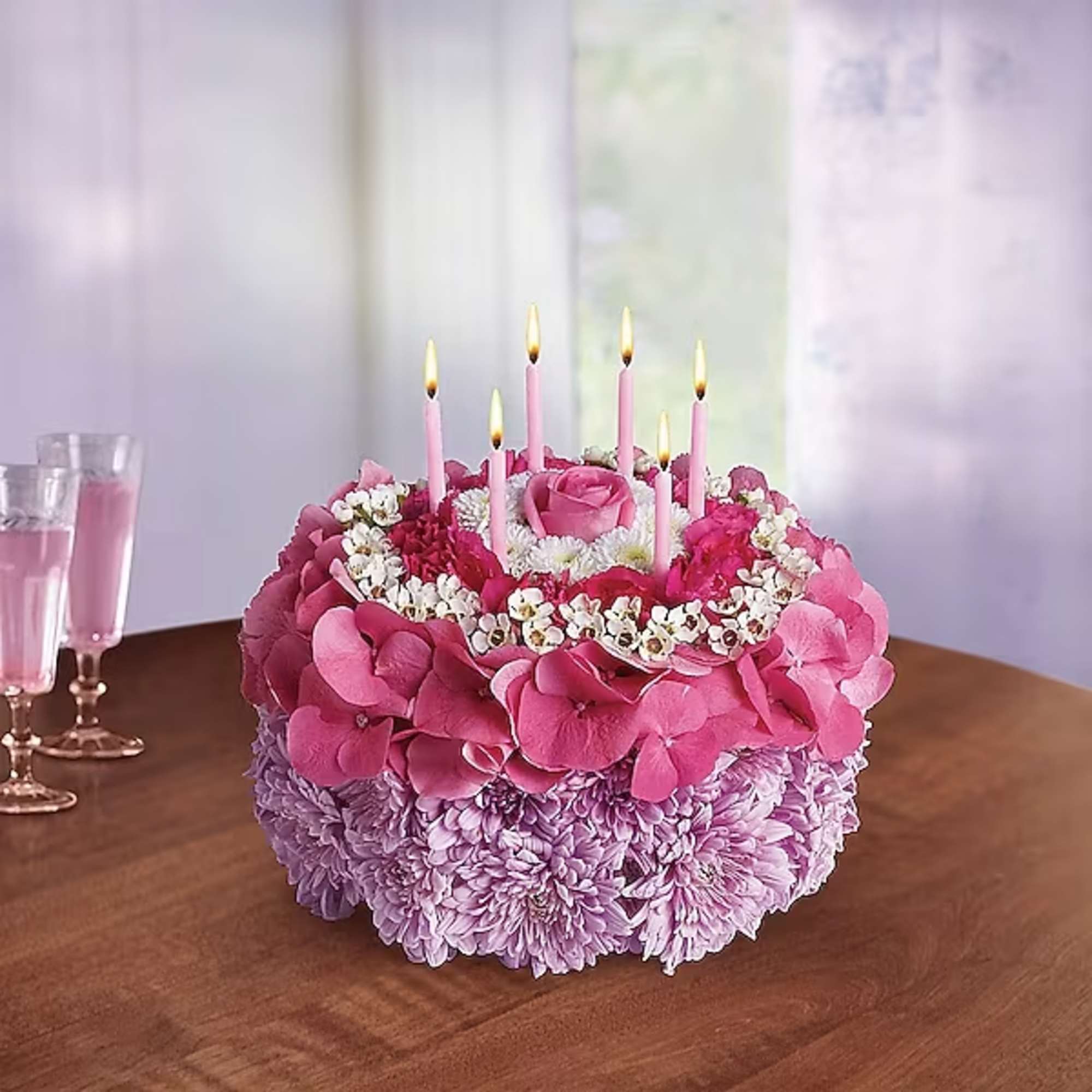 Pink and lavender floral cake with lit candles on a table