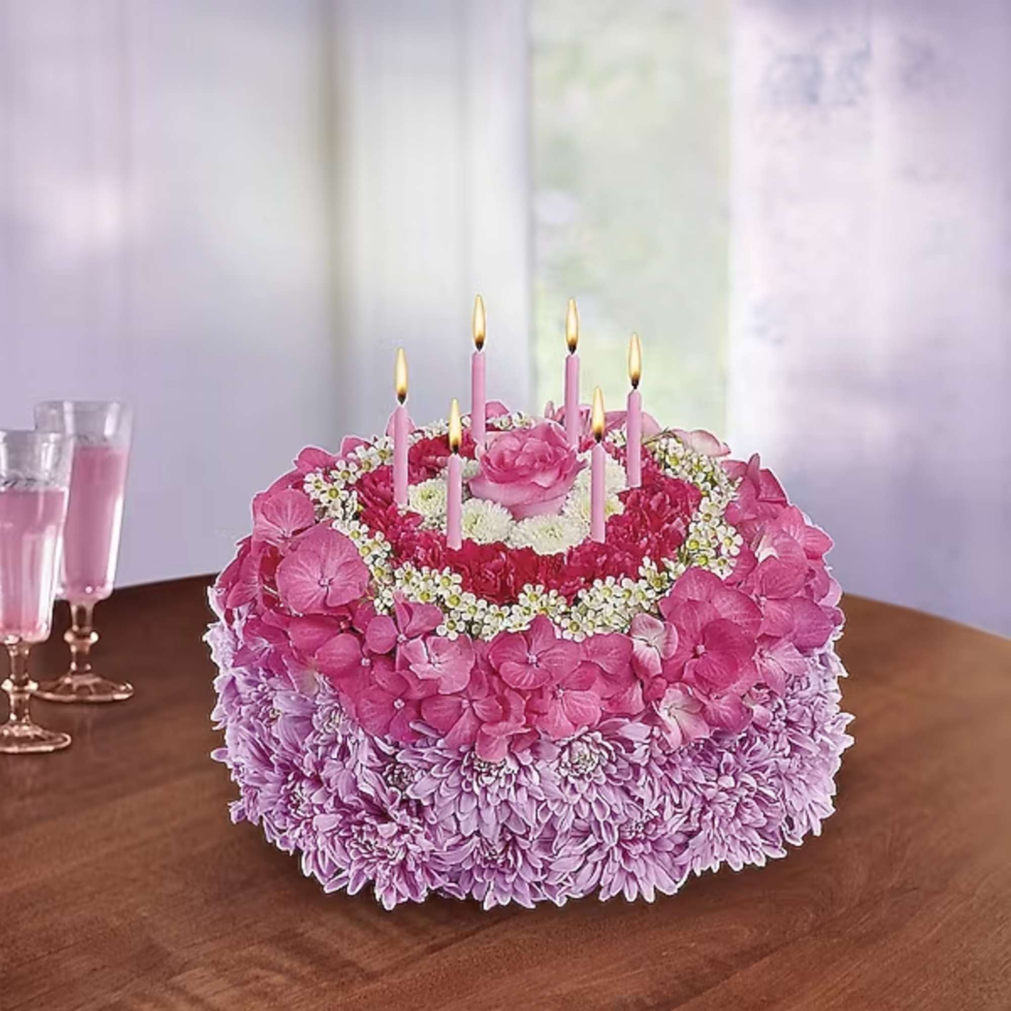 Pink floral cake with lit candles on a table
