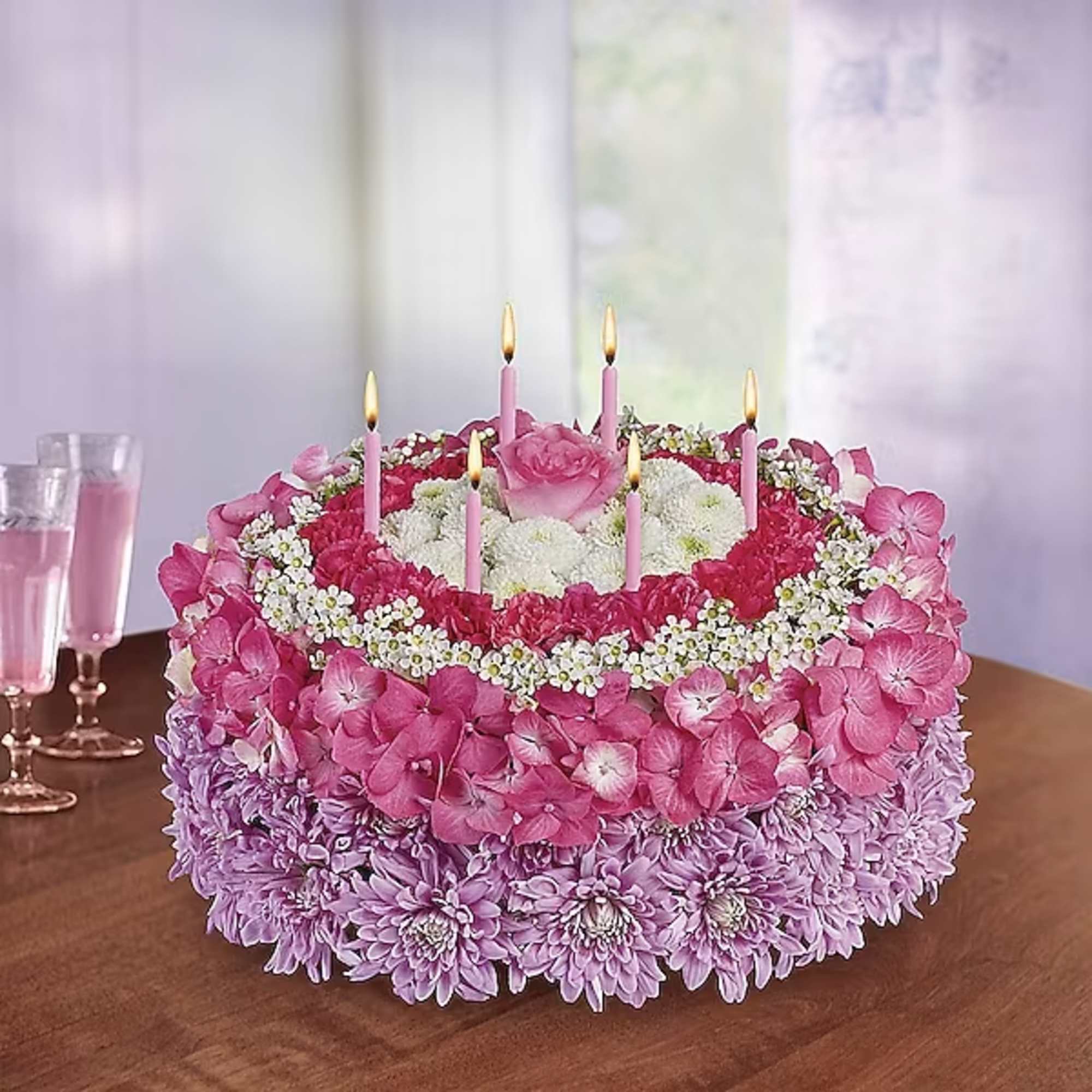 Round pink and lavender floral cake with lit candles on a table