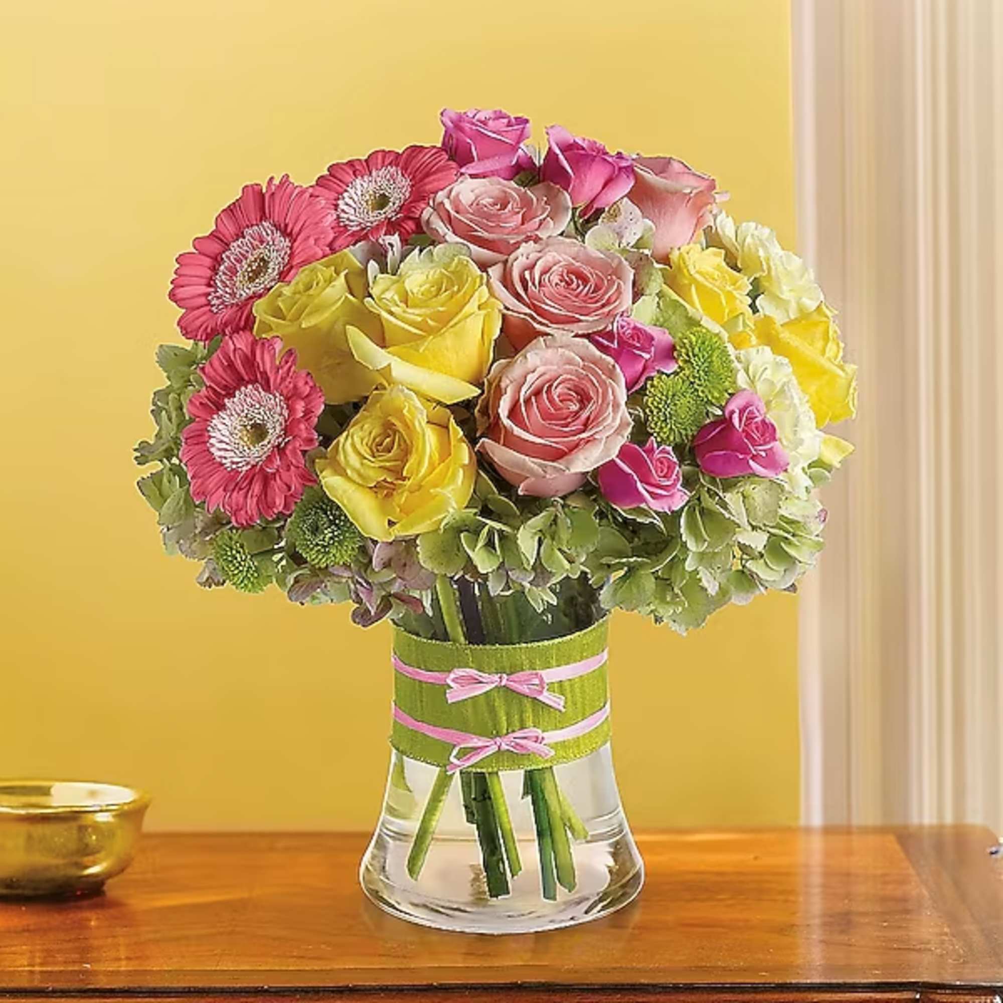 Bouquet of pink and yellow roses with gerbera daisies in a glass vase