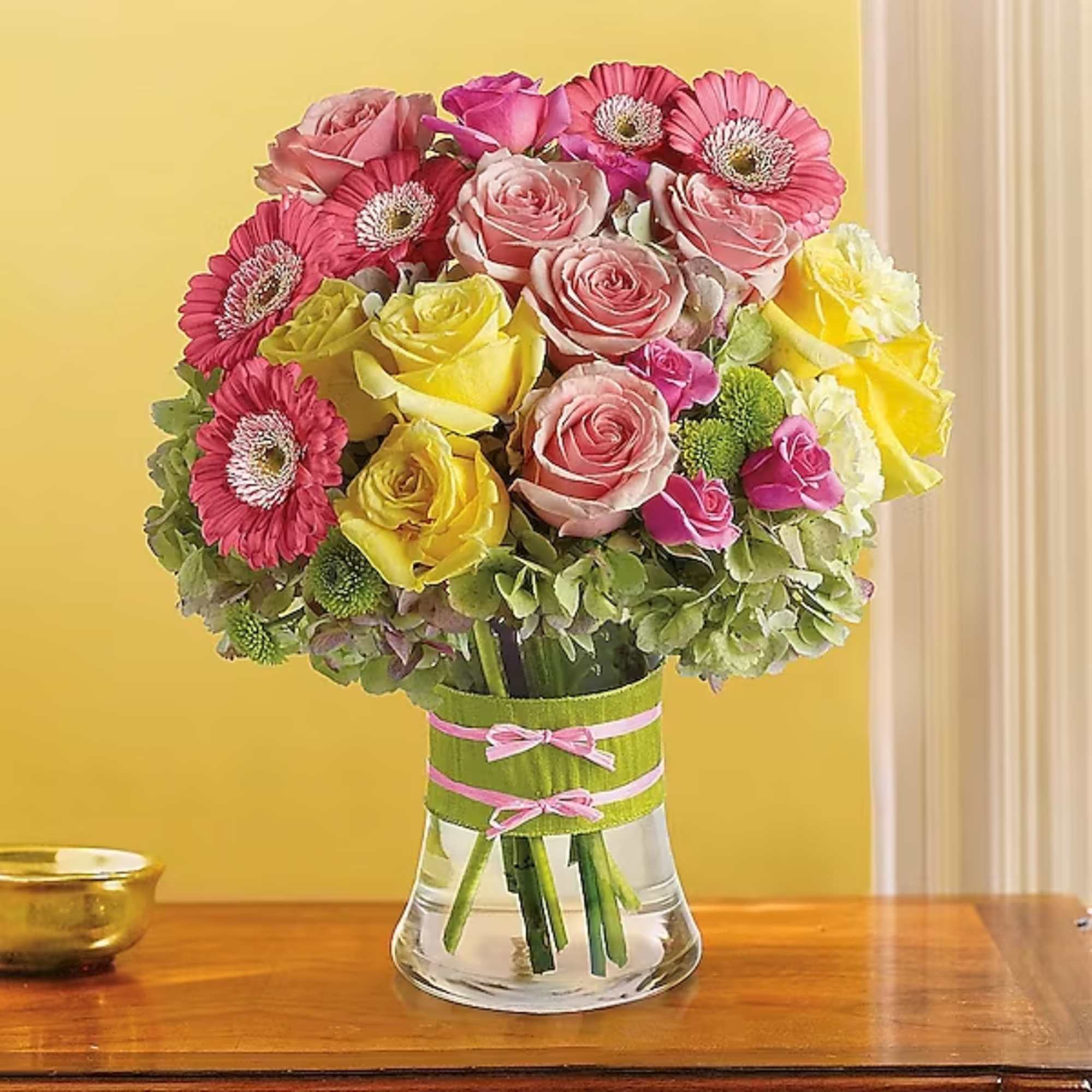 Bouquet of pink and yellow roses with pink gerbera daisies in a glass vase