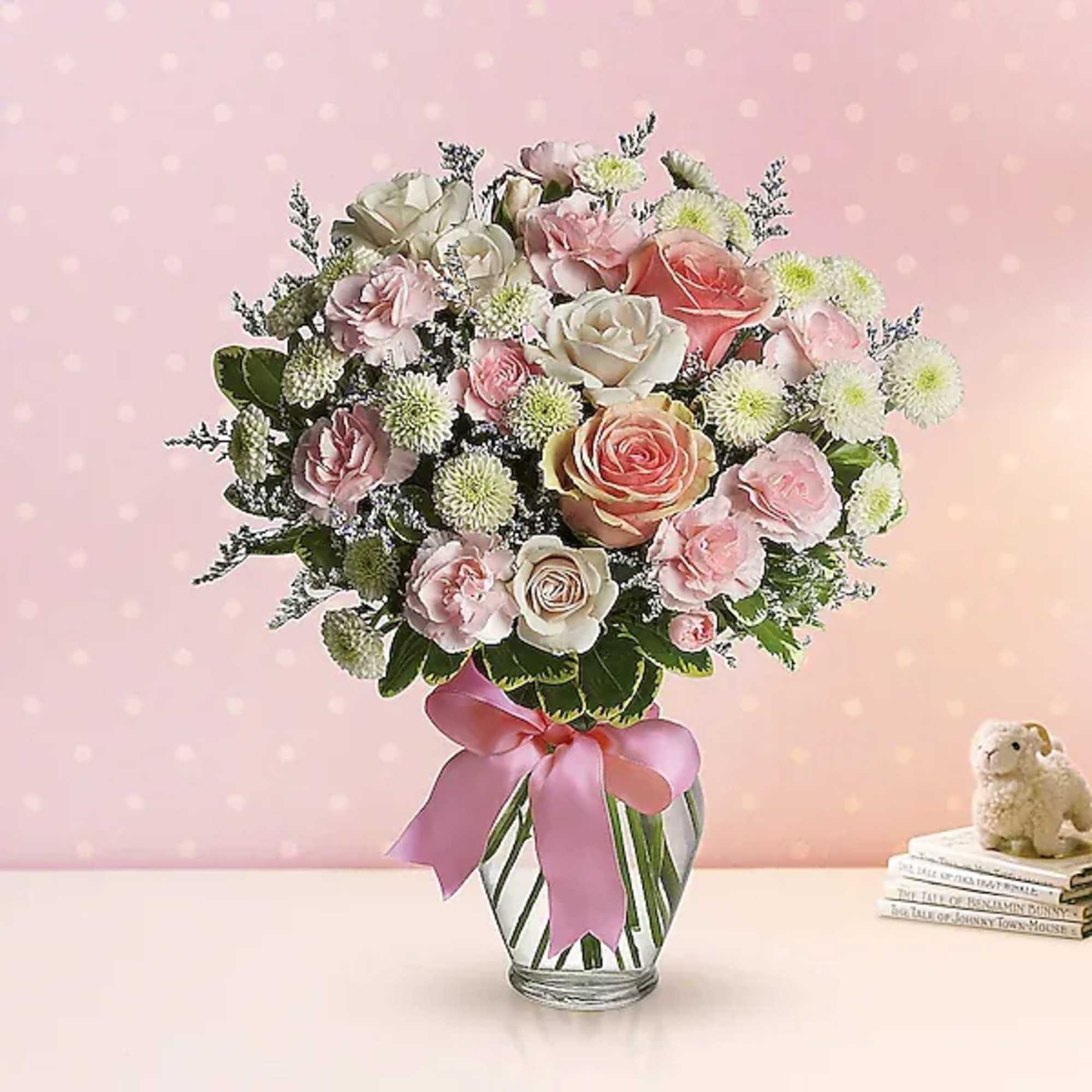 Pink and white bouquet of roses and carnations in a glass vase with a ribbon