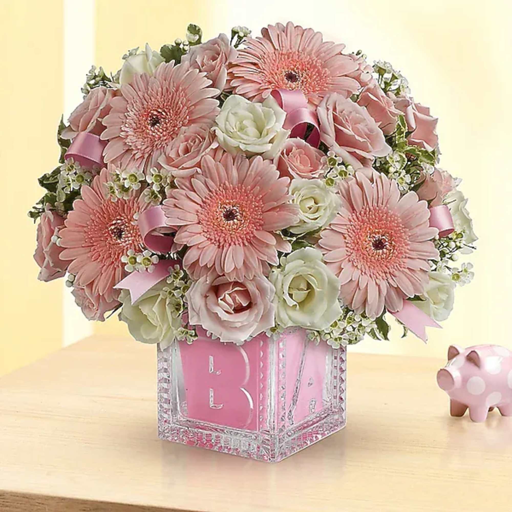 Pink and white bouquet in a clear block vase with a pink ribbon