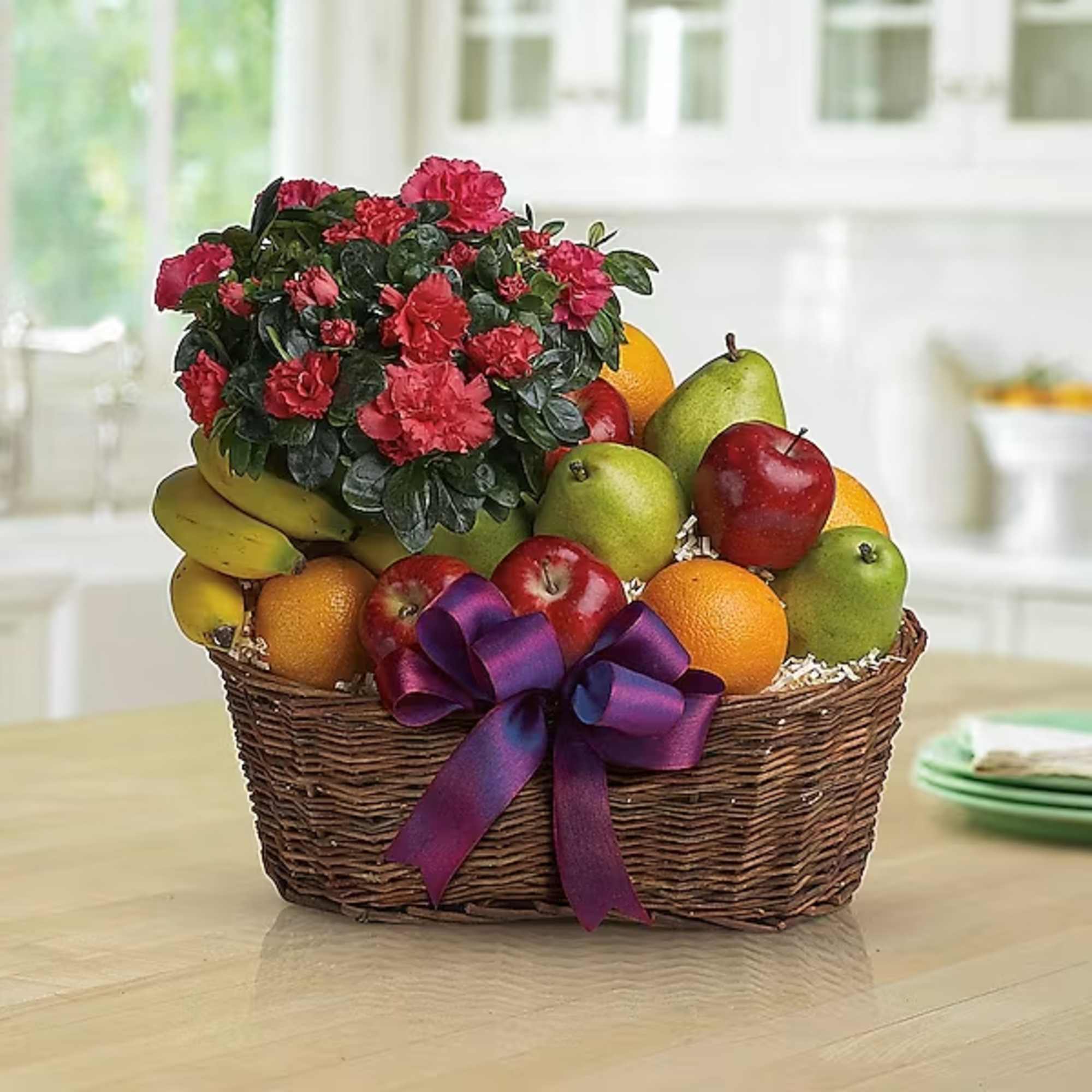 Fruit basket with a potted red flowering plant and a purple ribbon