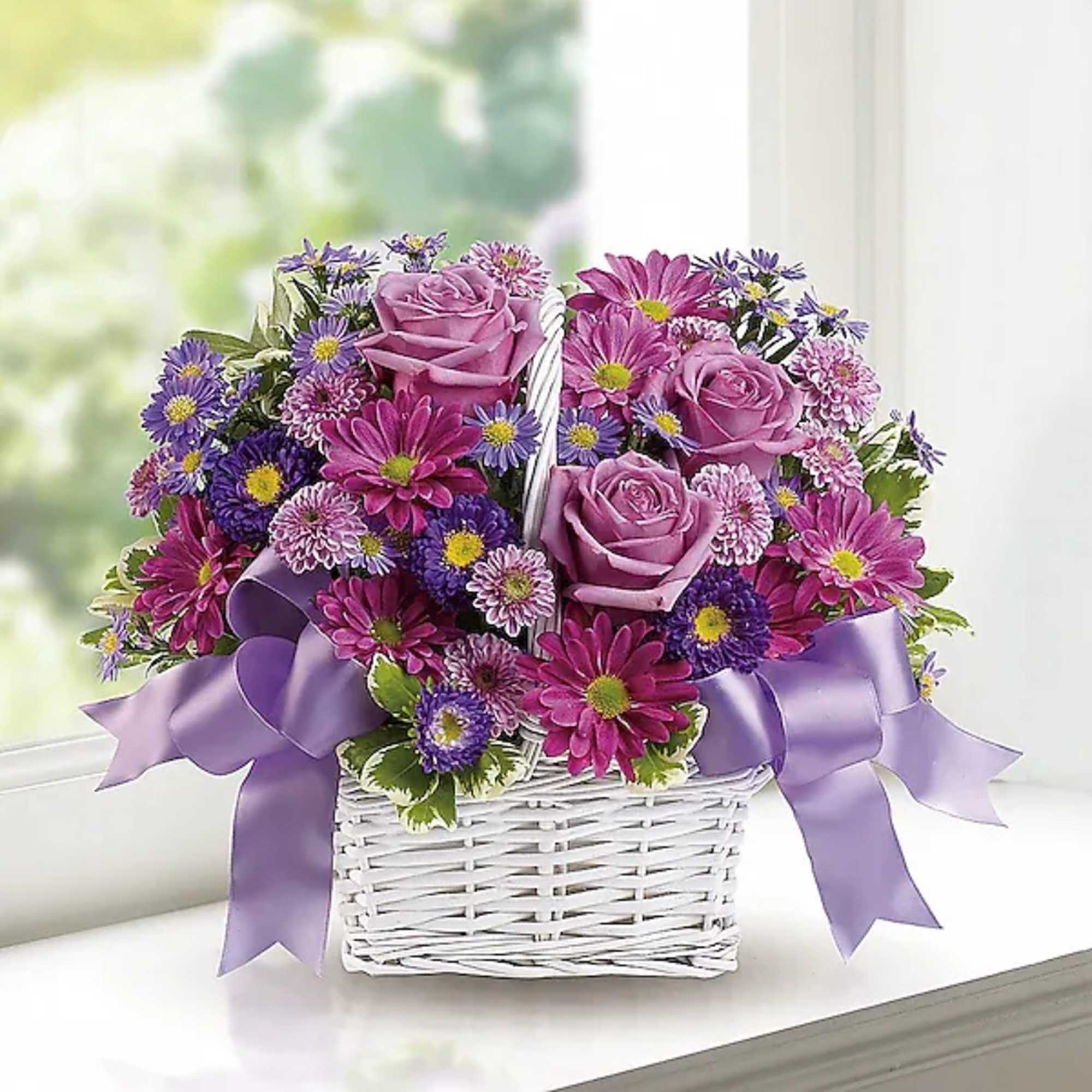 Purple and pink flower basket with roses and daisies in a white wicker basket
