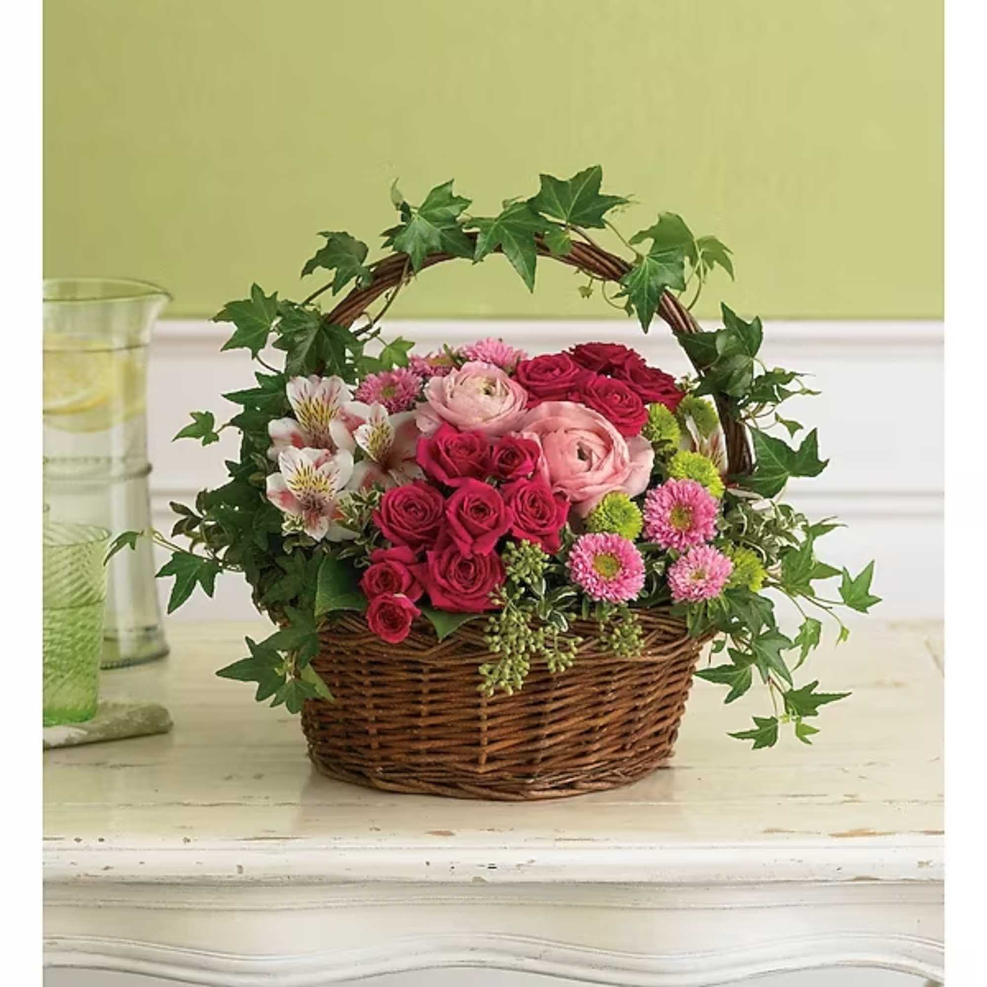 Basket arrangement of pink and red roses with daisies and ivy