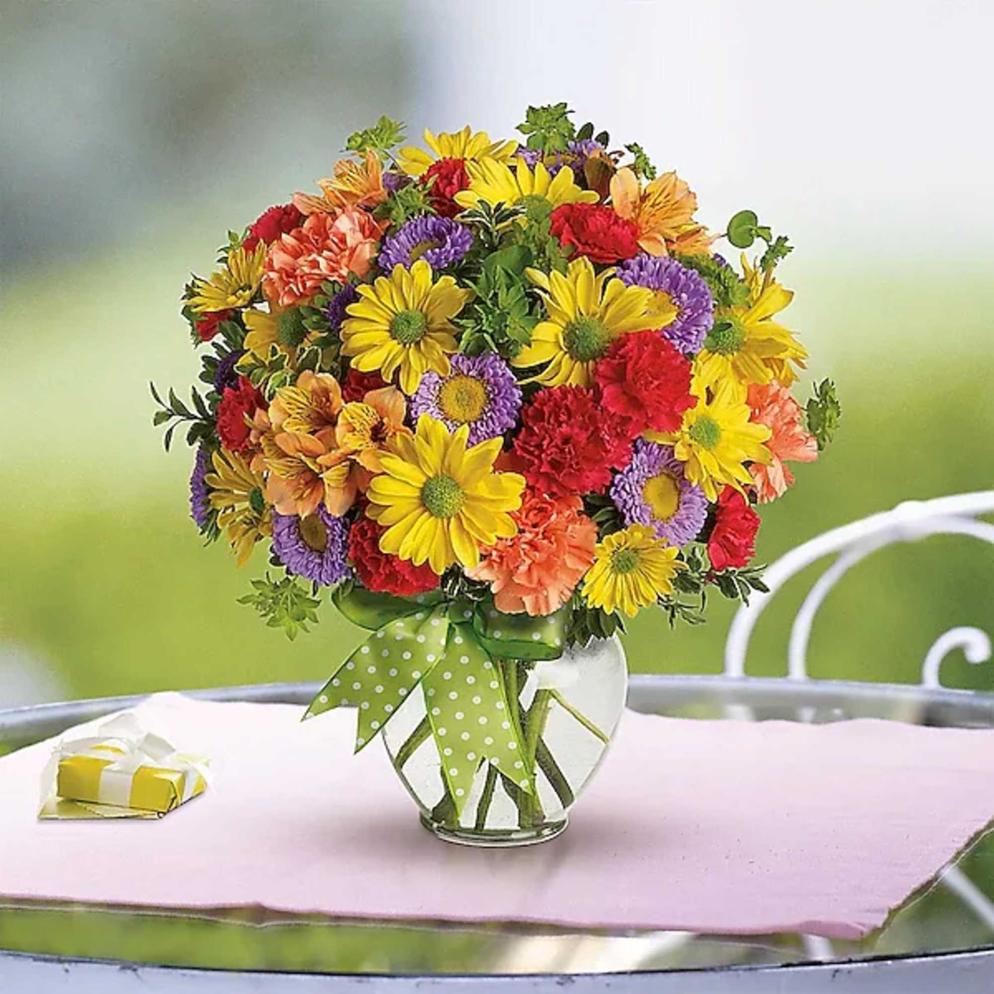 Colorful mixed flower bouquet in a glass vase with a green polka-dot ribbon