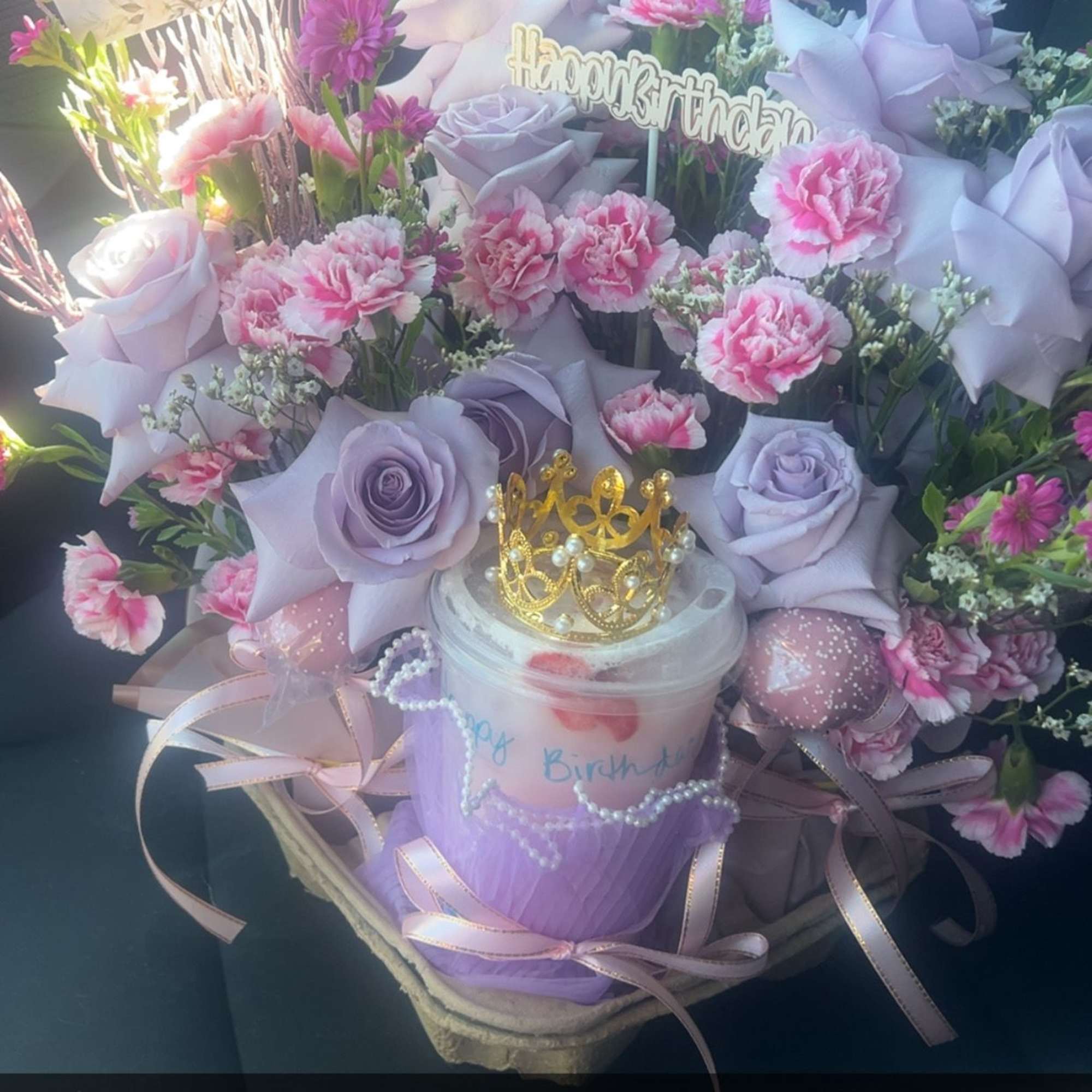 Lavender roses and pink carnations arranged around a drink cup with a crown topper