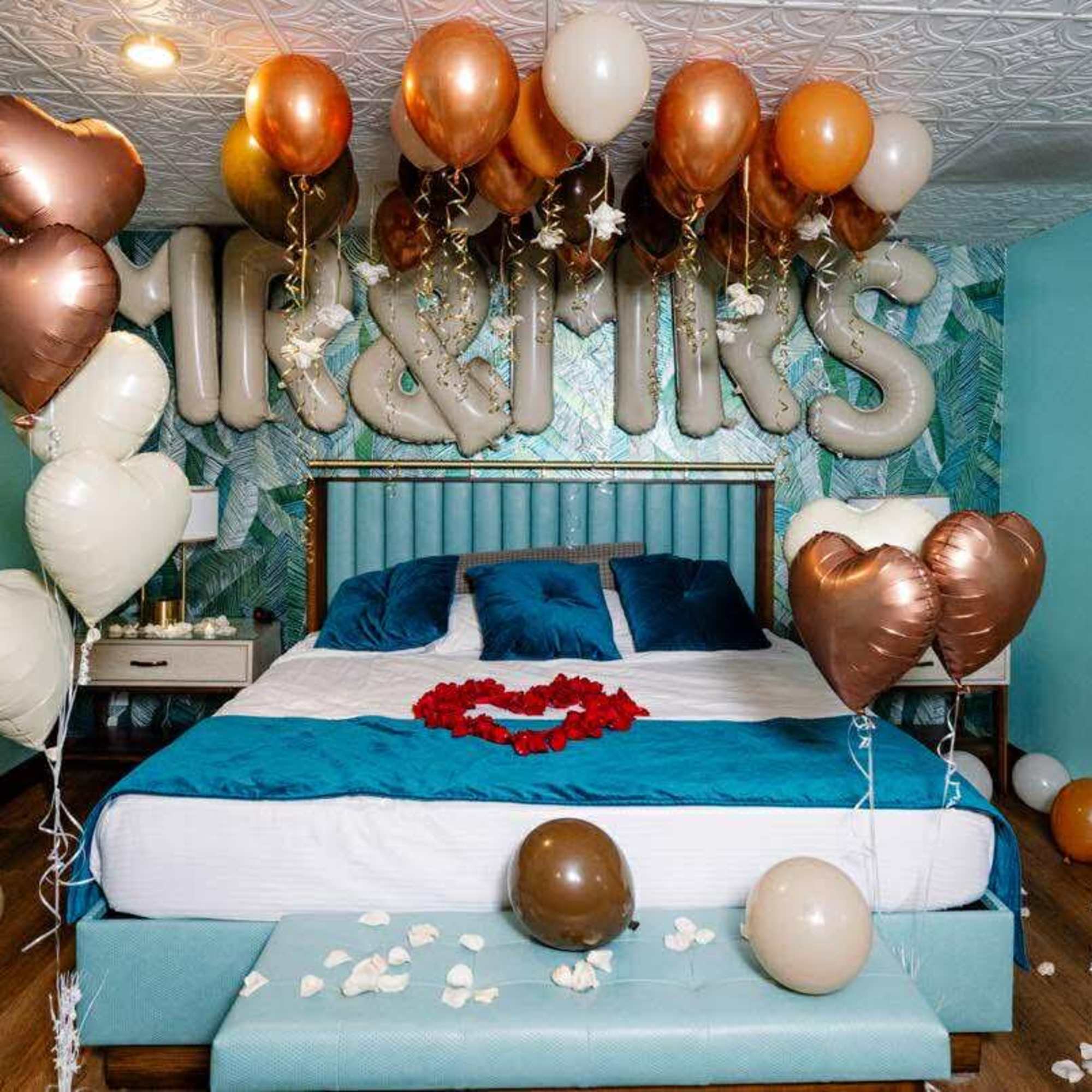 Bedroom decorated with heart-shaped balloons and rose petals on the bed