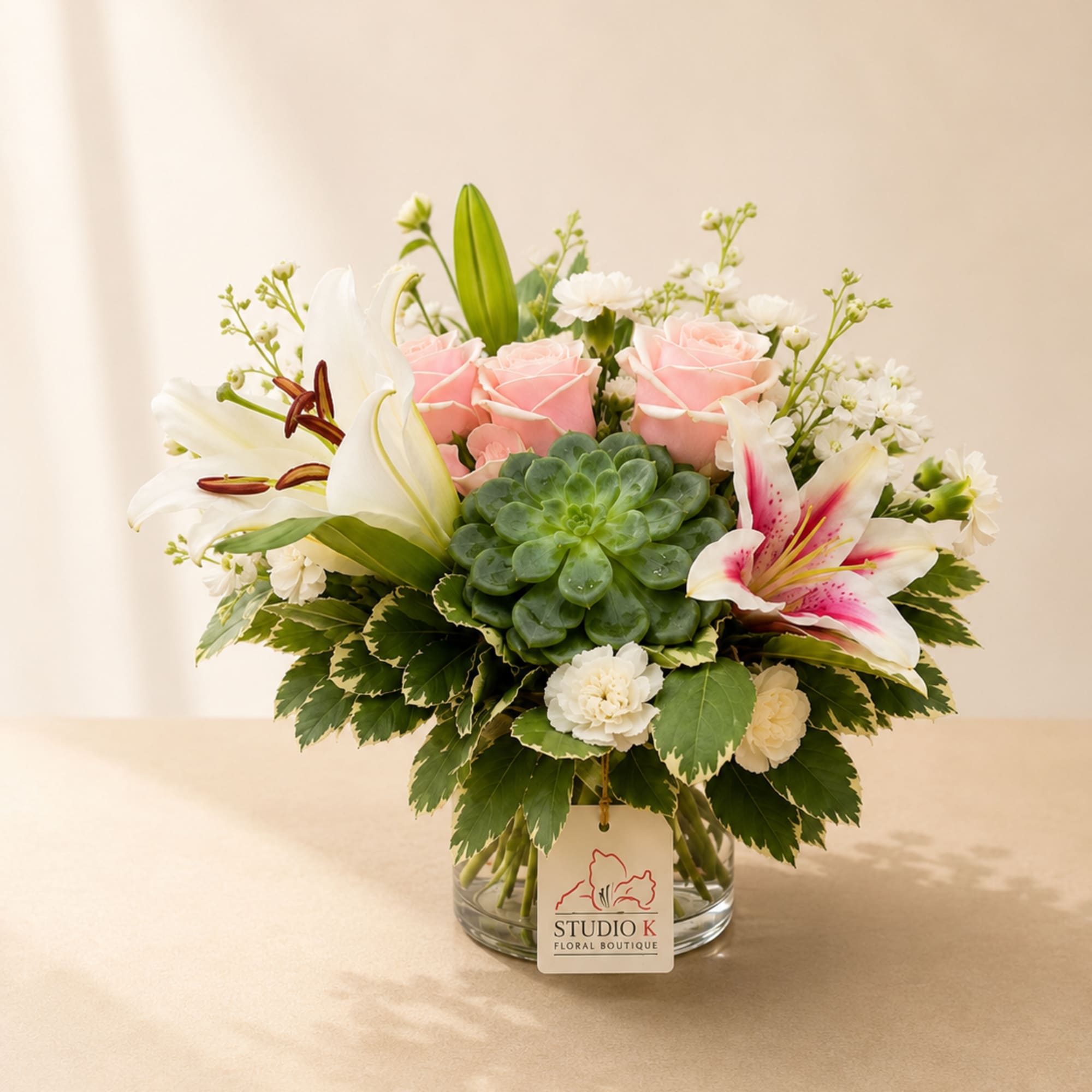 Pink roses and white lilies arranged with a green succulent in a glass vase