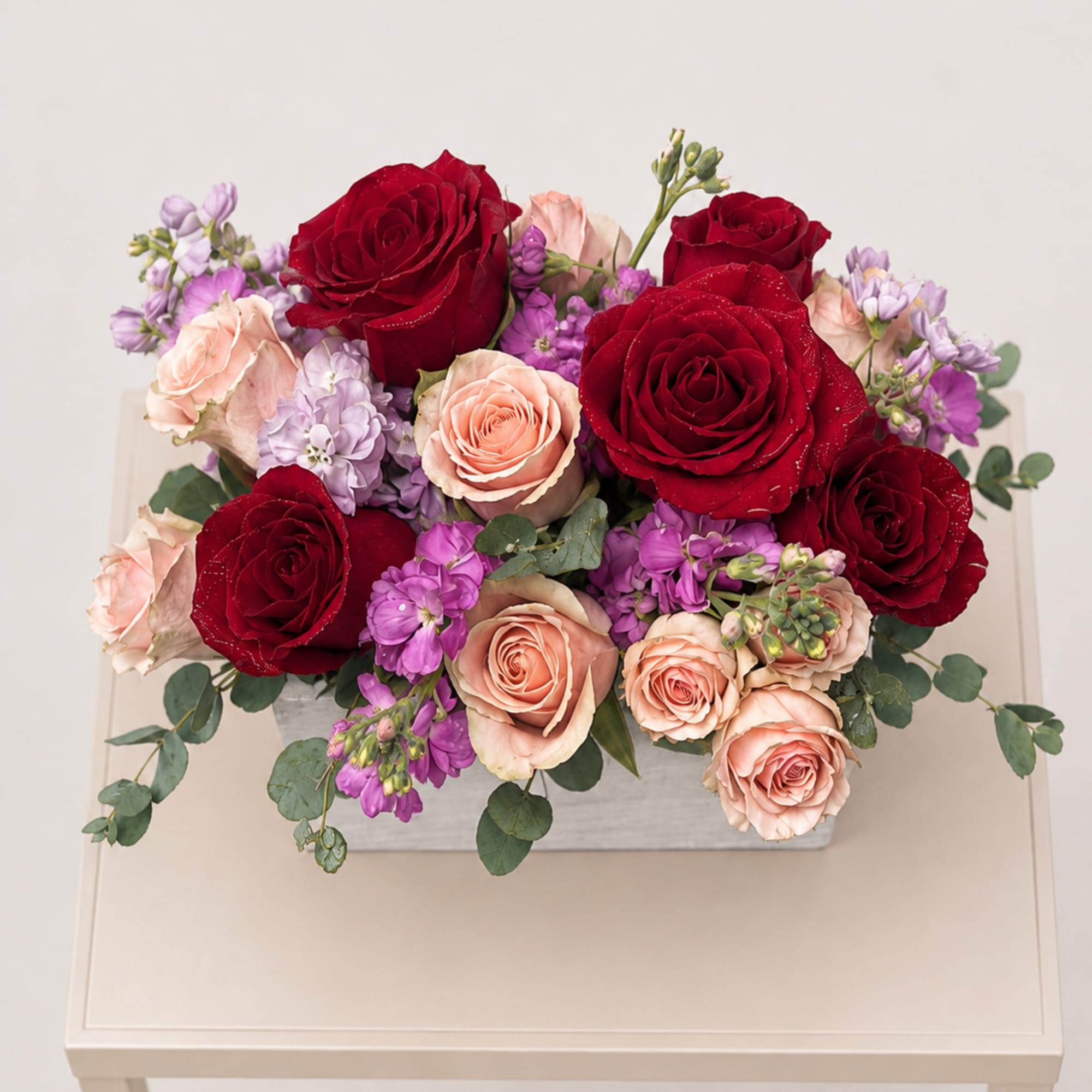 Mixed bouquet of red, blush, and lavender flowers in a rectangular box