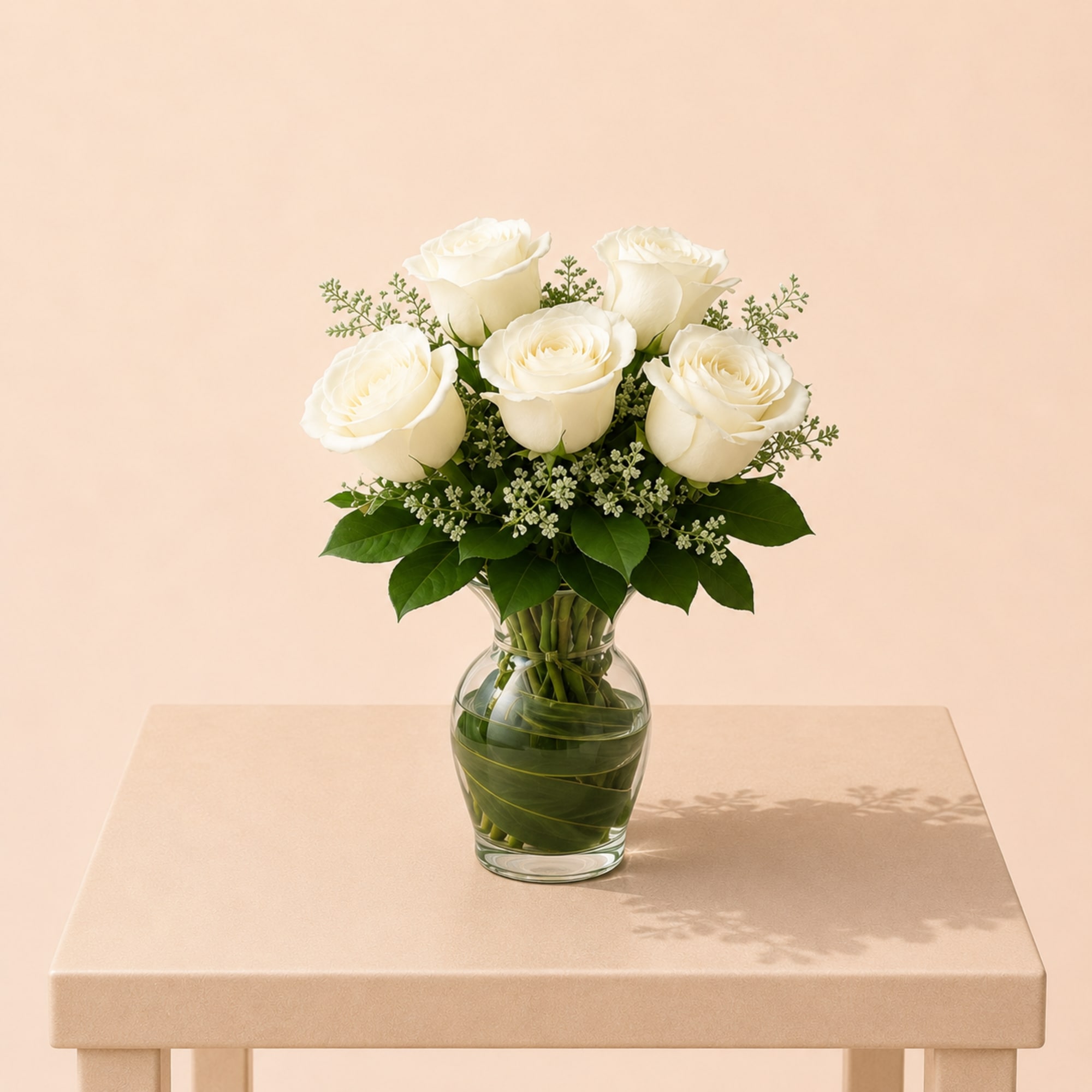 White roses arranged in a clear glass vase with greenery