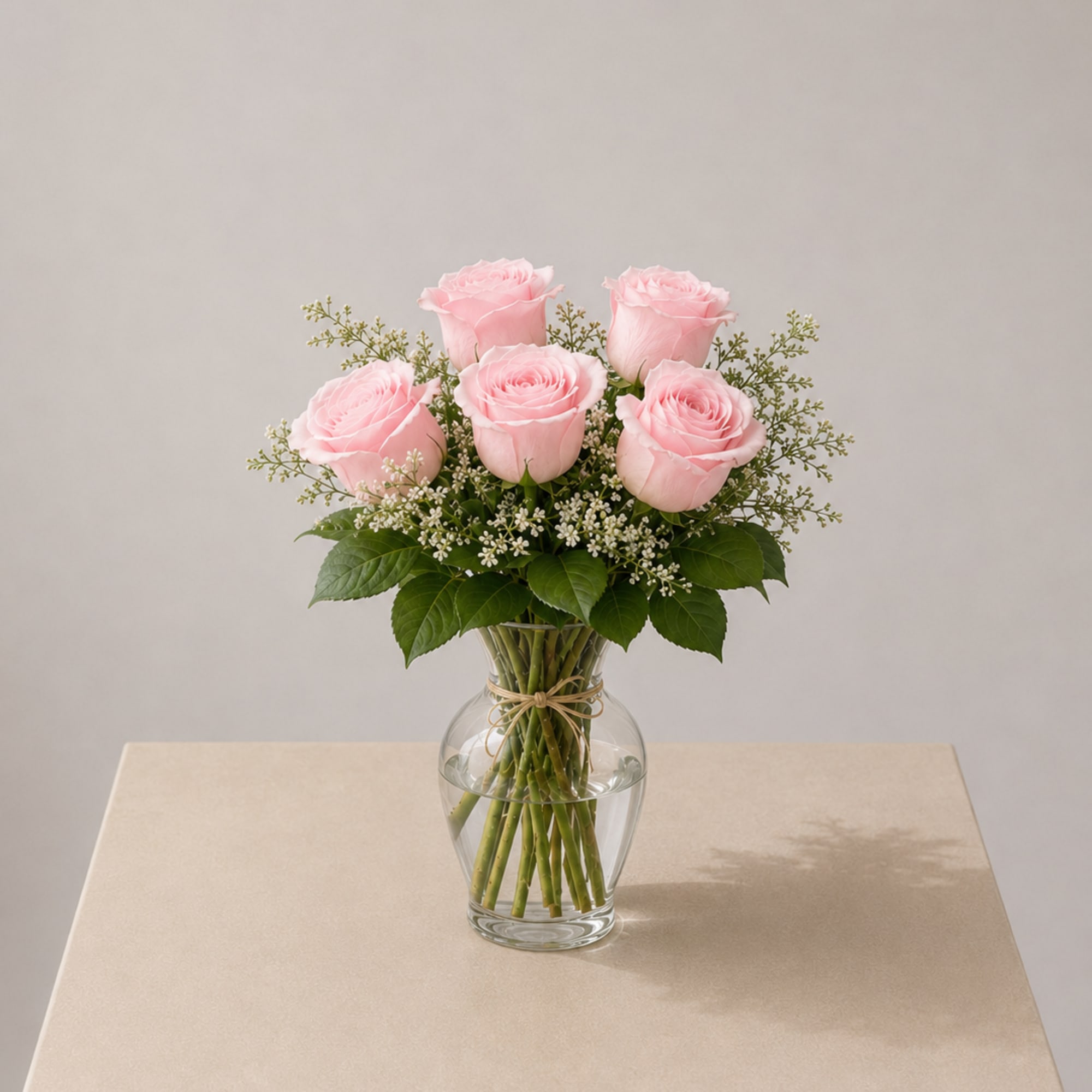 Soft blush roses beautifully arranged in a clear glass vase, accented with