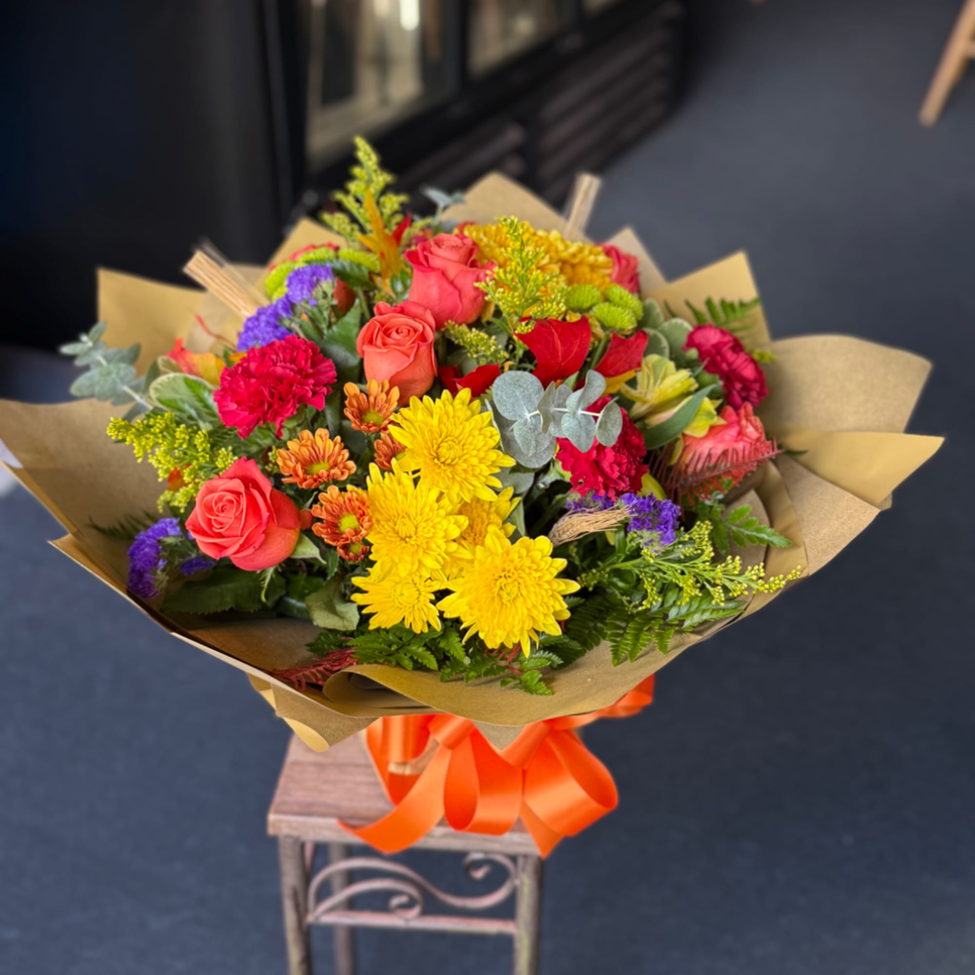 Mixed bouquet of roses, chrysanthemums, and carnations wrapped in kraft paper