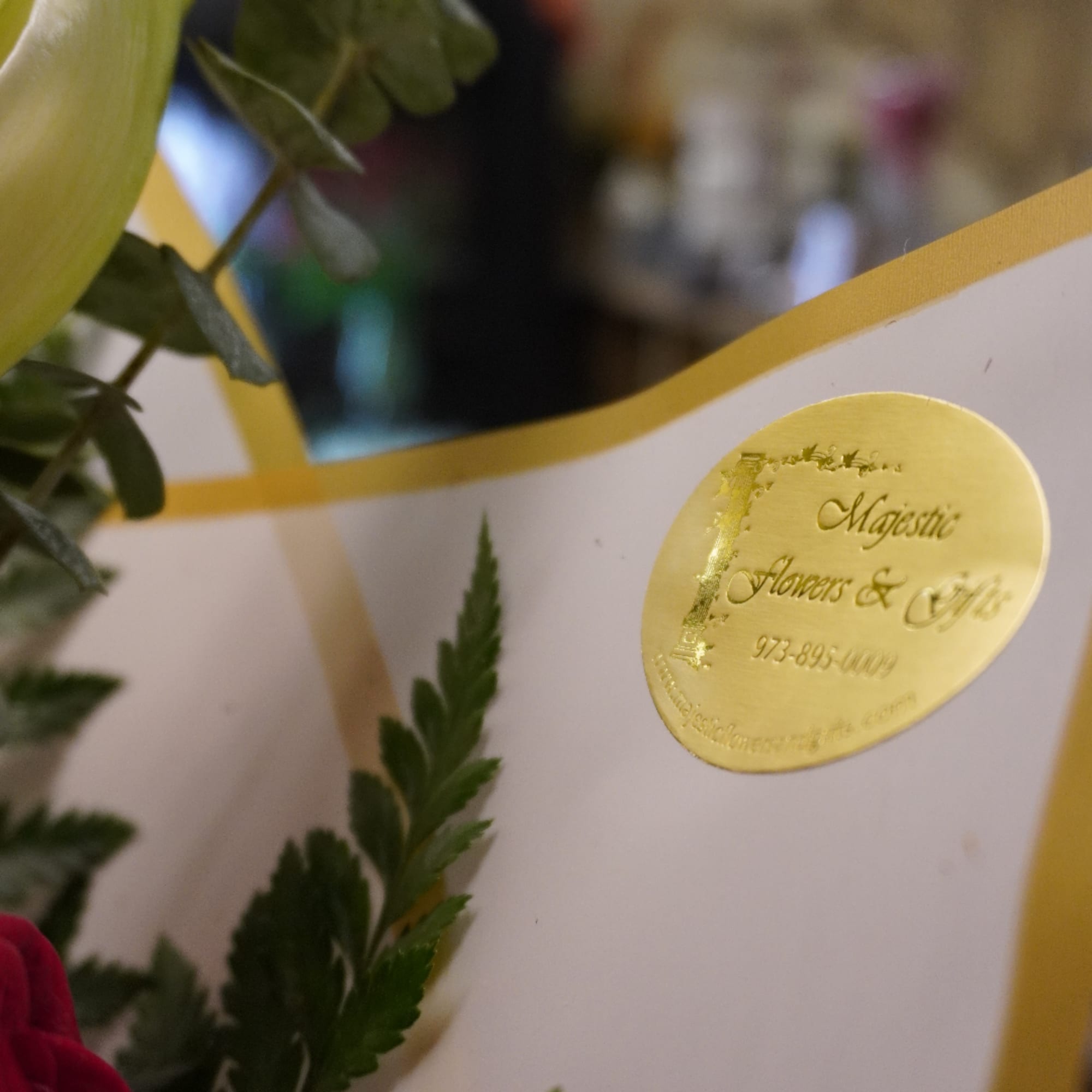 Close-up of a floral arrangement with pink blooms and greenery beside a gold logo sticker.