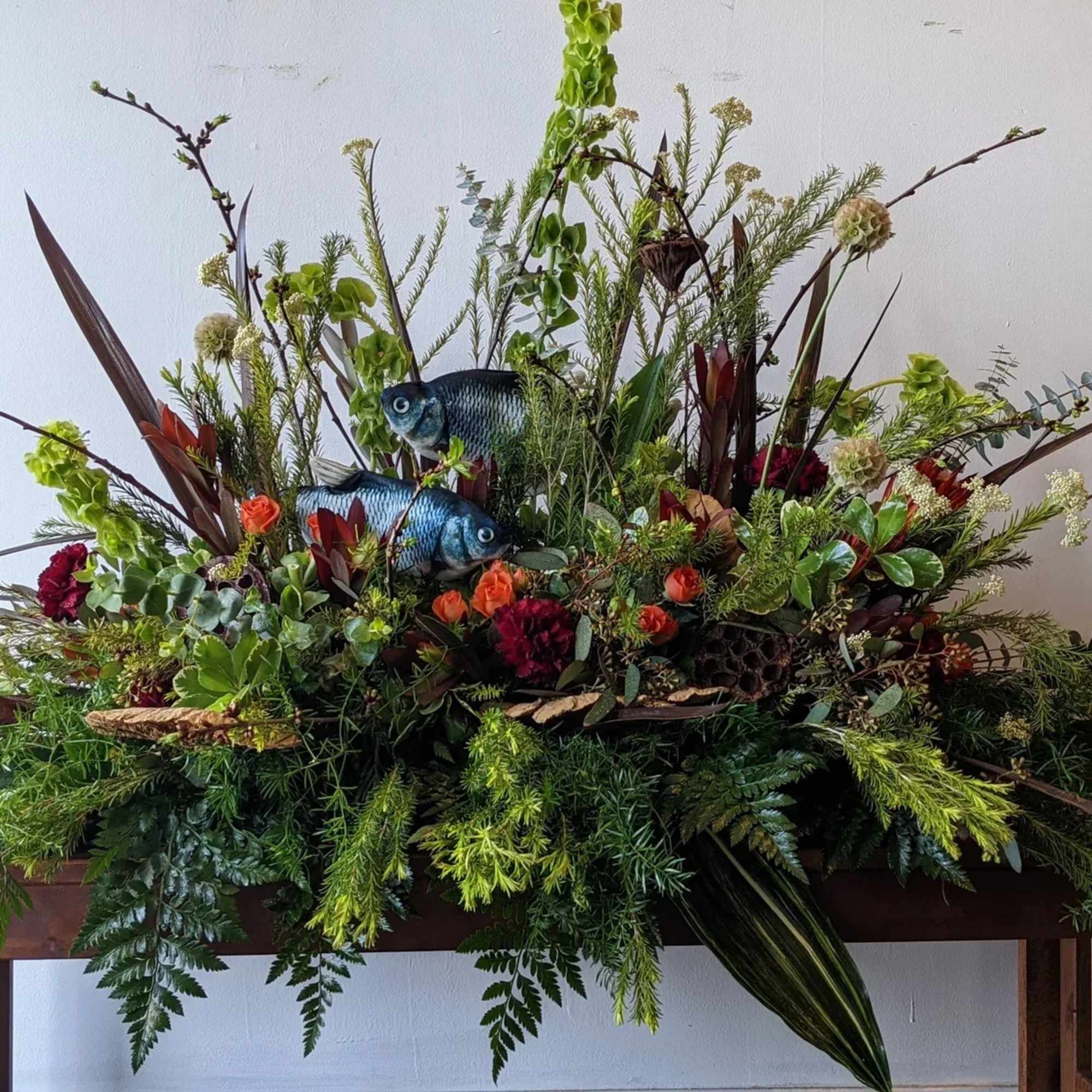 Large floral arrangement with greenery, orange blooms, and two decorative fish