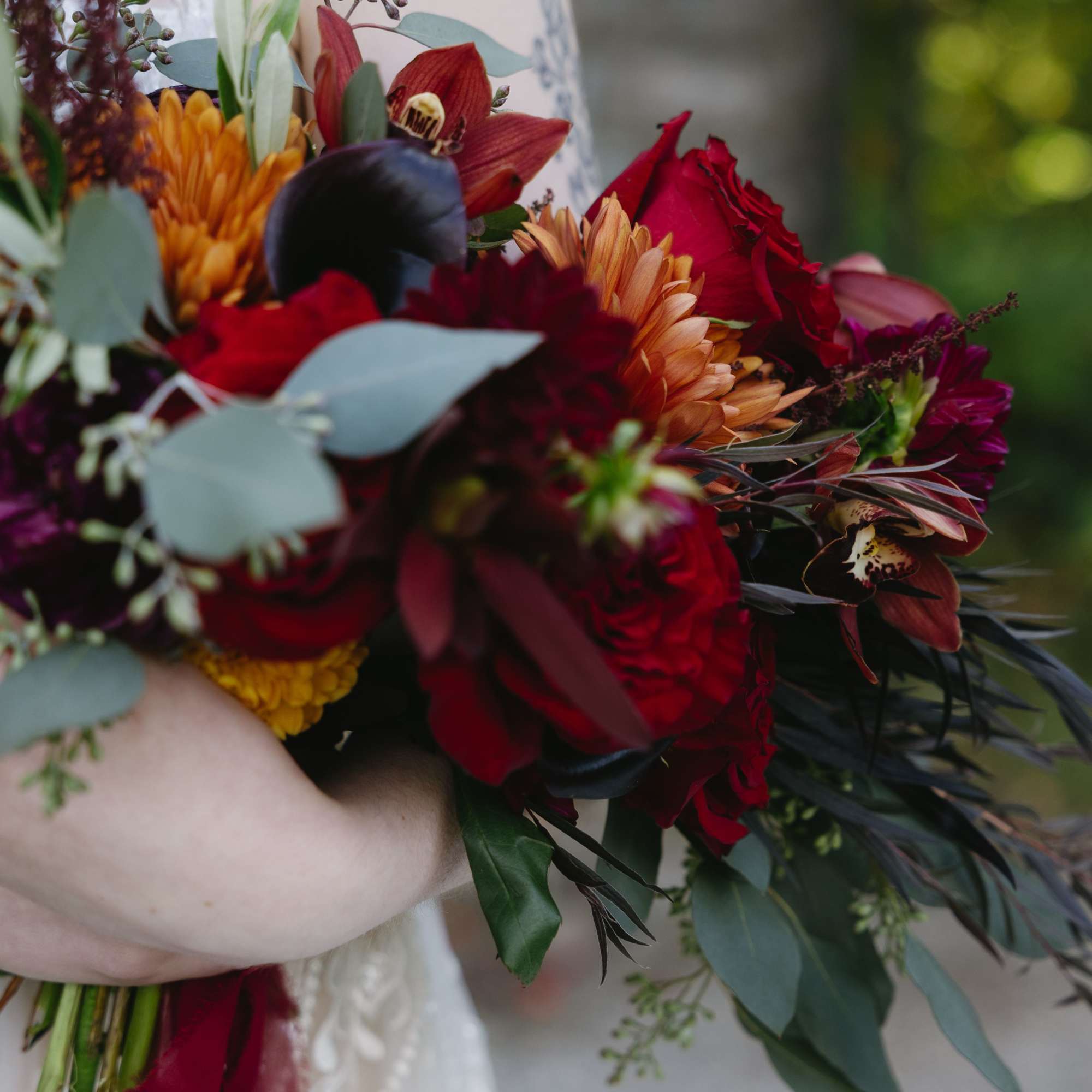Bride holding a bouquet of red, orange, and burgundy flowers