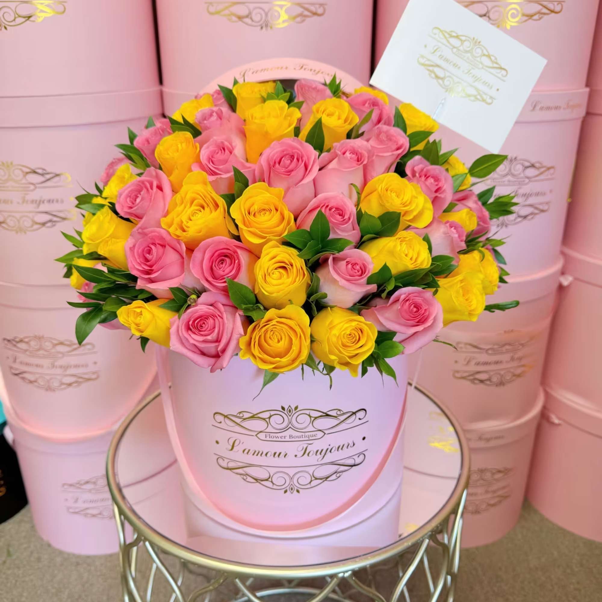 Pink and yellow roses arranged in a round pink hat box