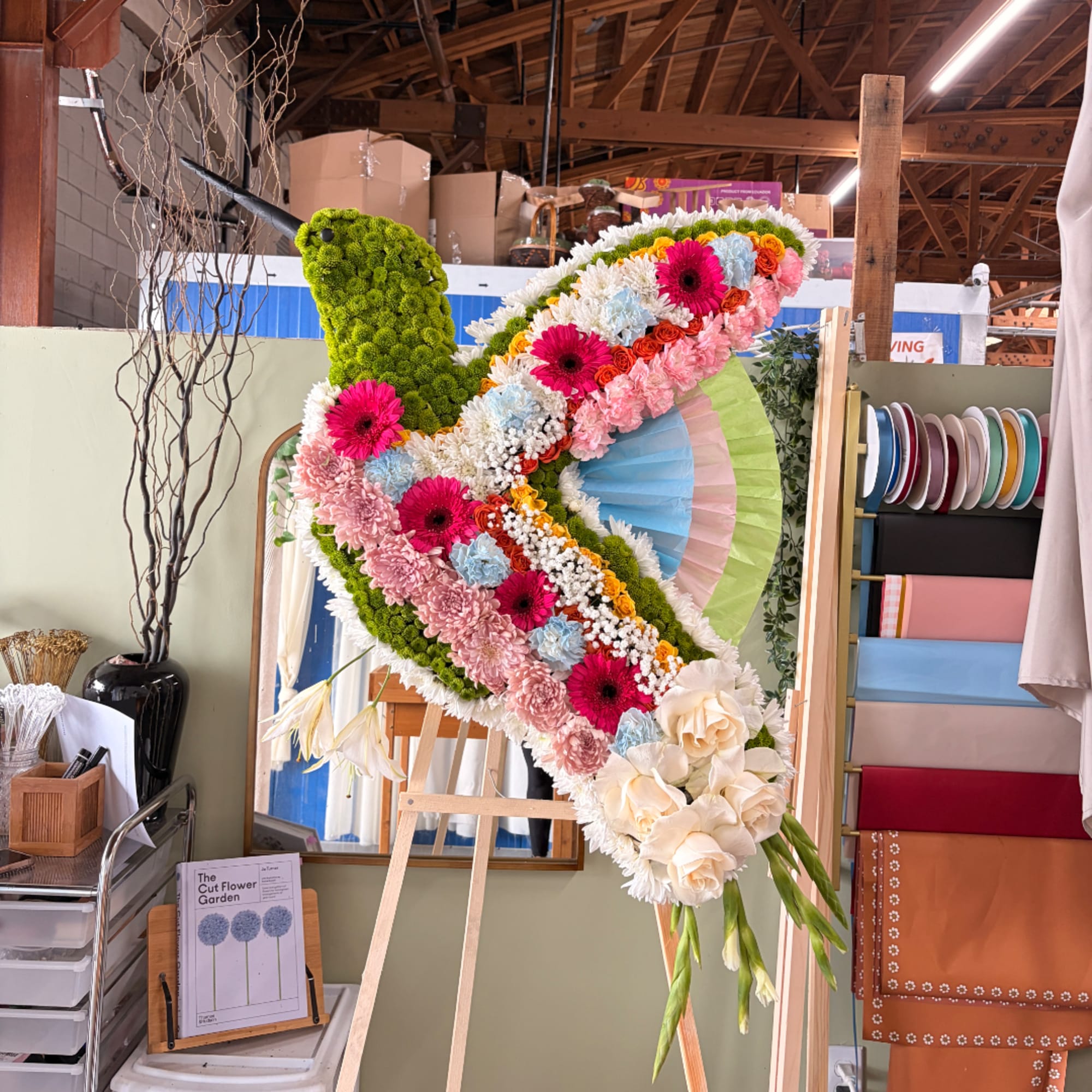 Large floral bird sculpture on an easel with pink, white, and blue flowers