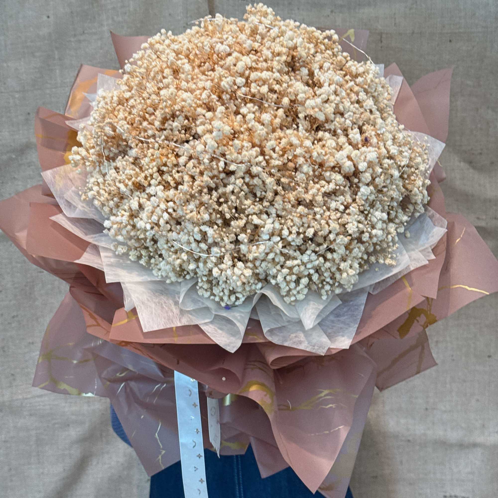 Large bouquet of tiny white flowers wrapped in pink and white paper