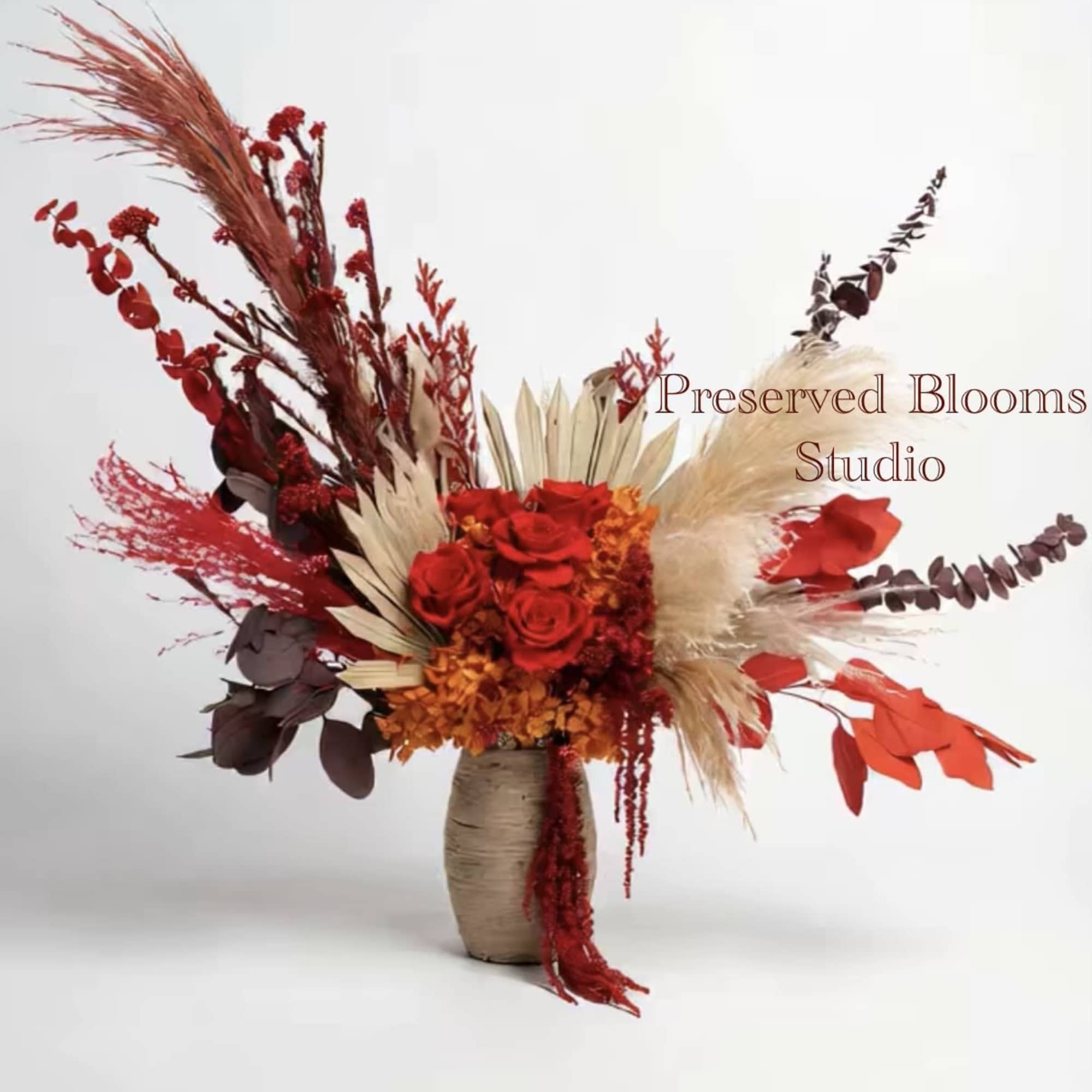 Tall asymmetrical arrangement of red roses and dried botanicals in a neutral ceramic vase