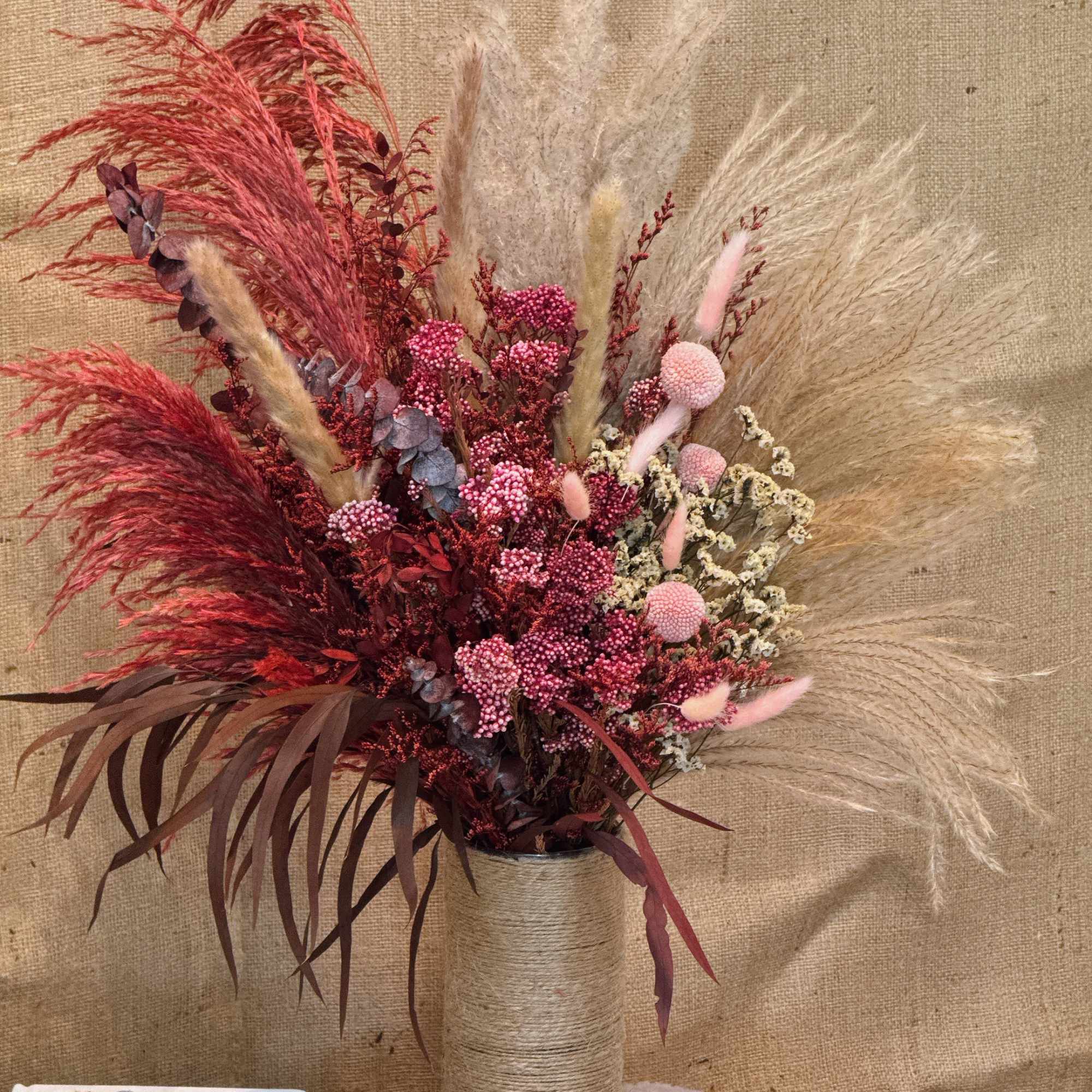 Tall dried red and beige pampas-style arrangement in a twine-wrapped cylinder vase