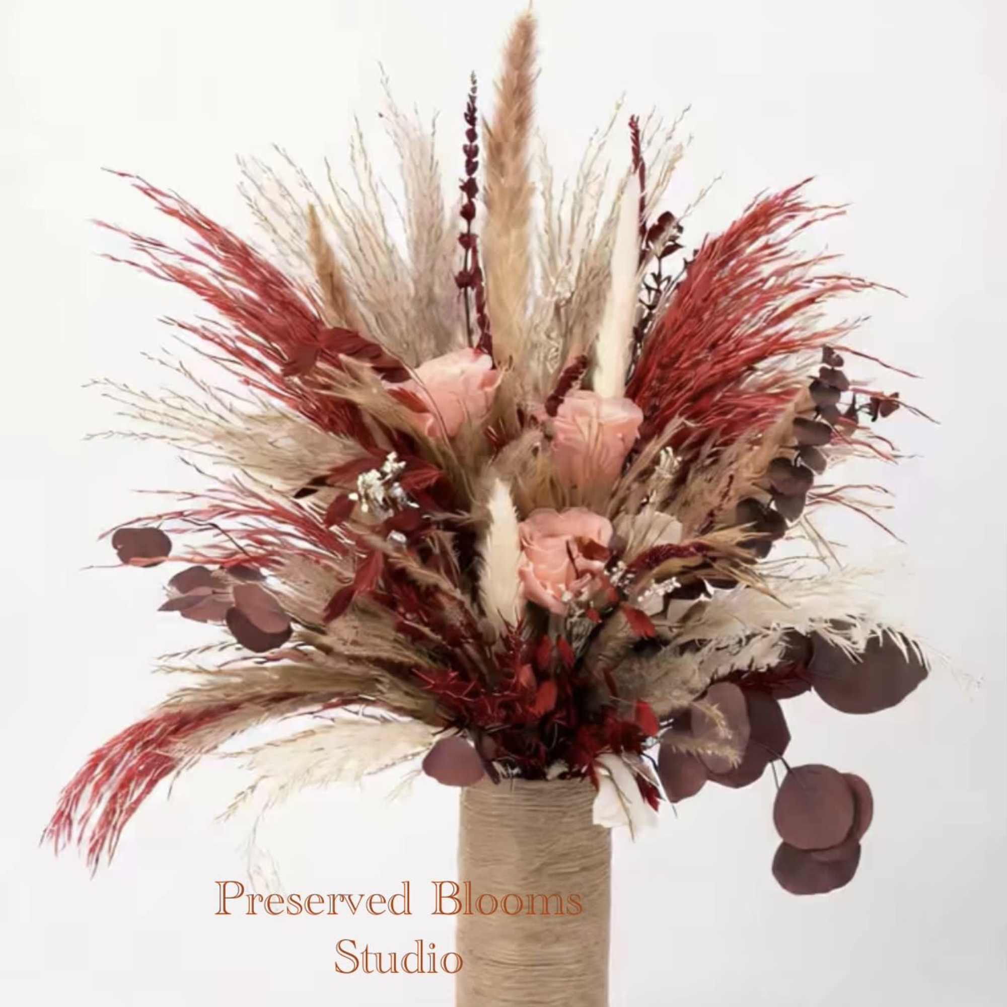 Tall dried arrangement with peach roses, red and tan pampas plumes in a twine-wrapped cylinder vase