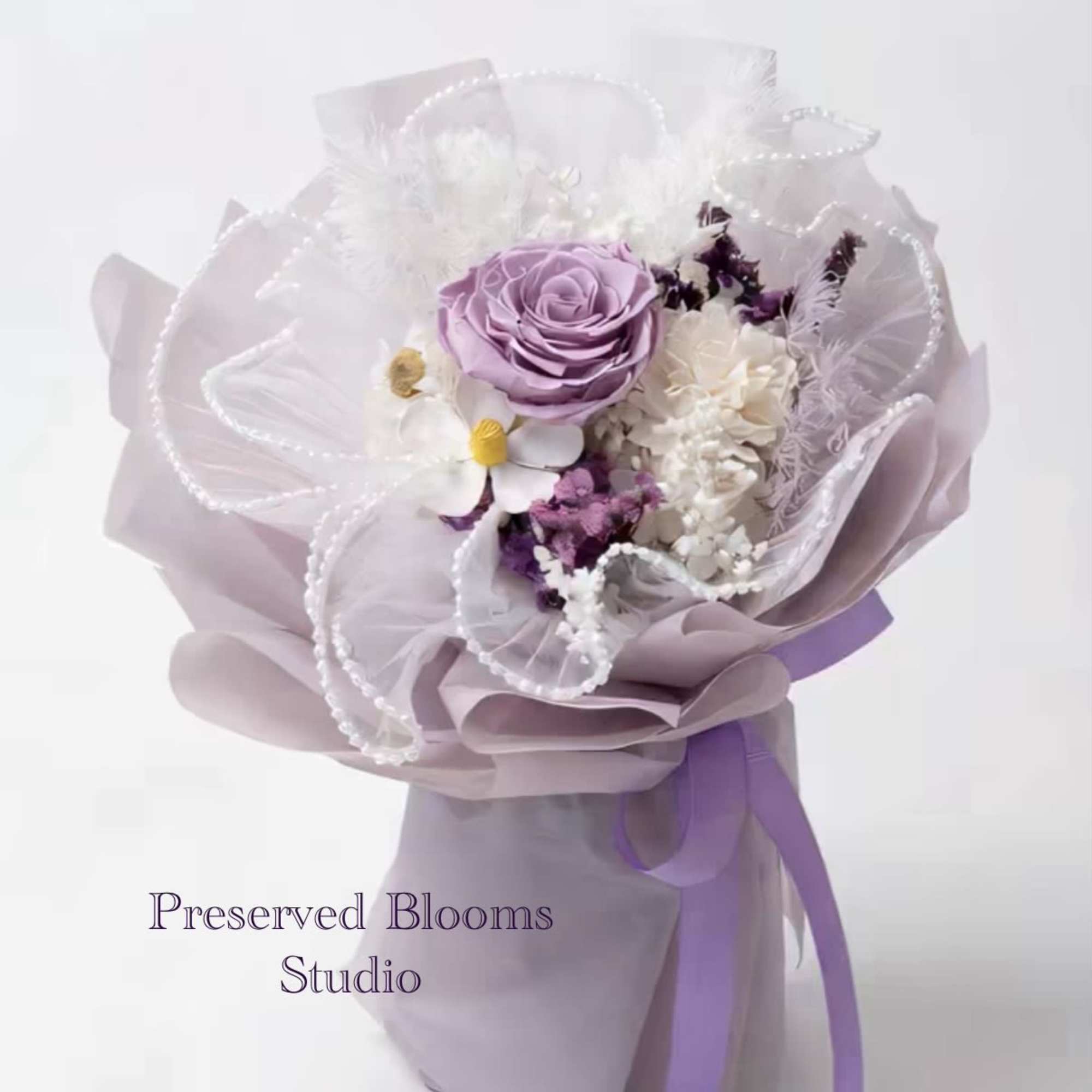 Hand-tied bouquet of lavender and white flowers wrapped in lilac paper with pearl accents and ribbon.