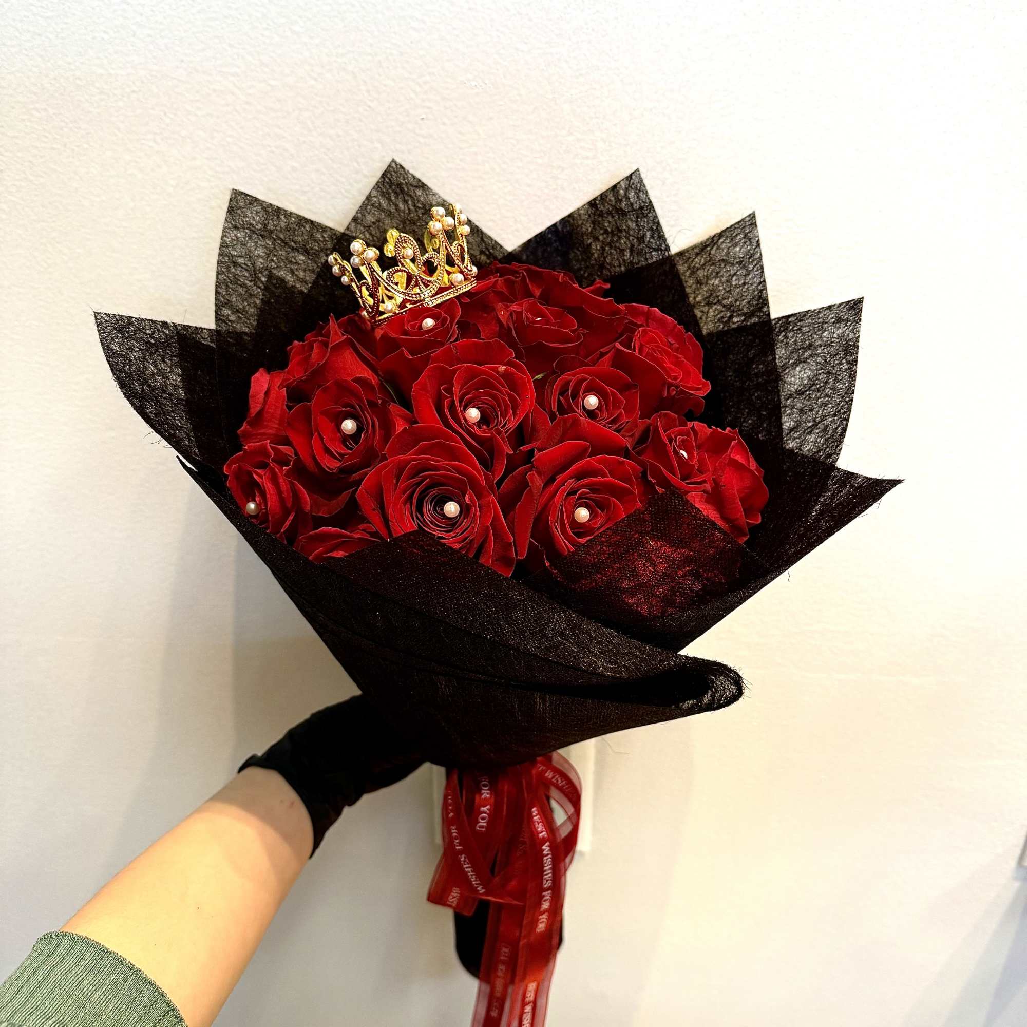 Bouquet of red roses wrapped in black paper with a small crown topper