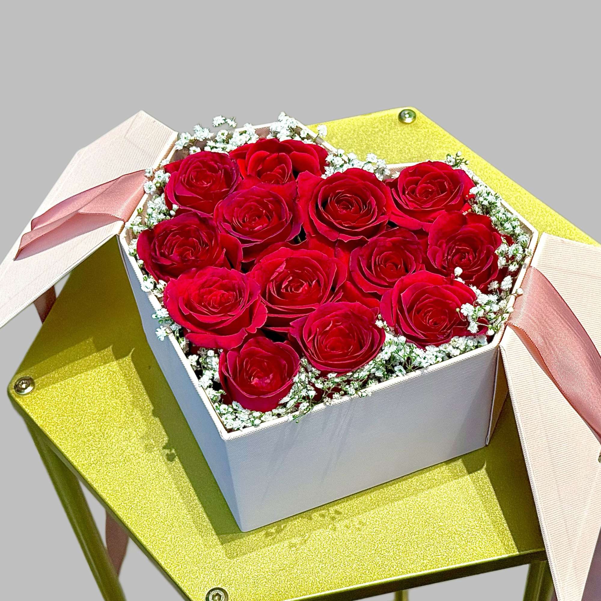 Box of red roses with pink ribbons on a gold stand