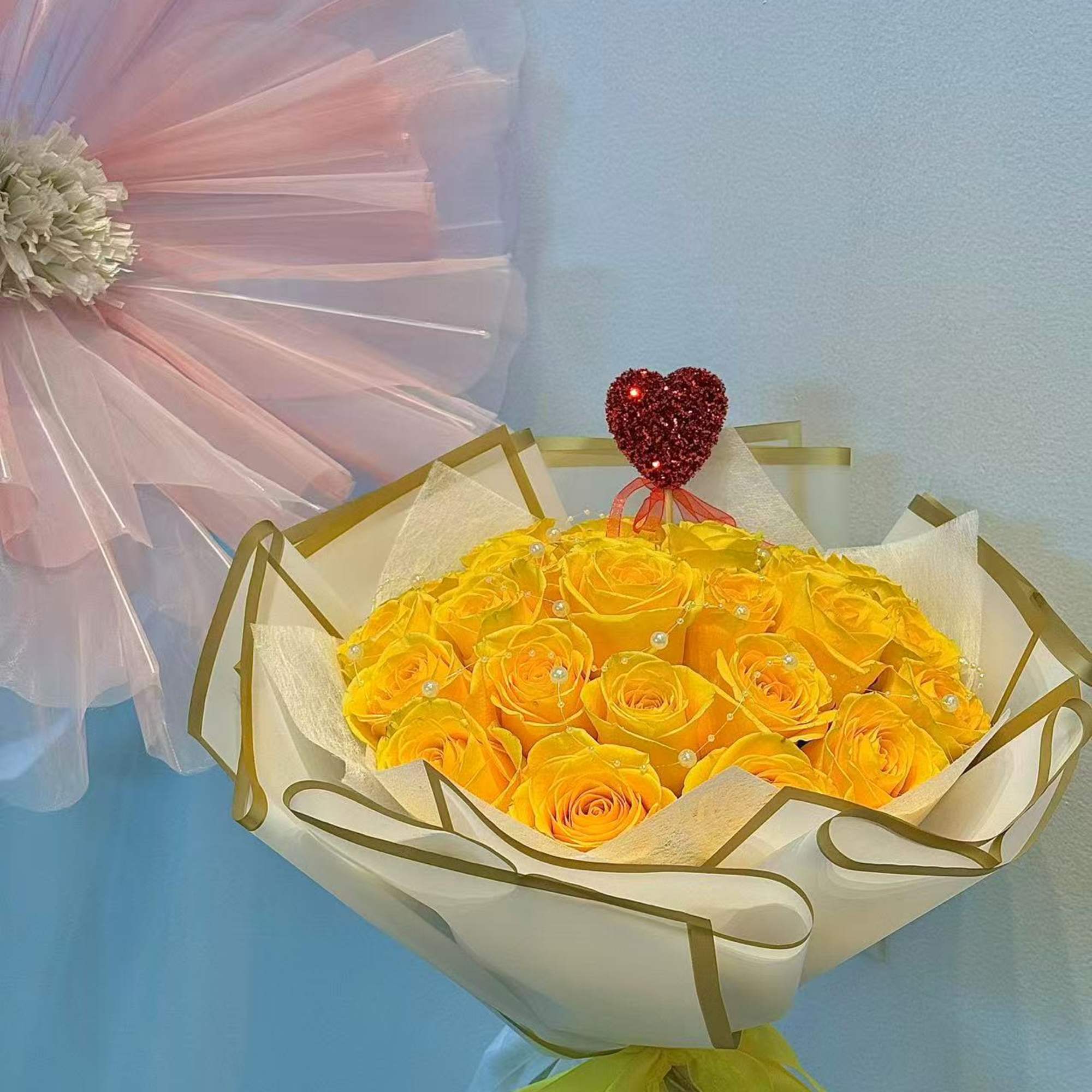 Bouquet of yellow roses wrapped in white paper with a red heart topper