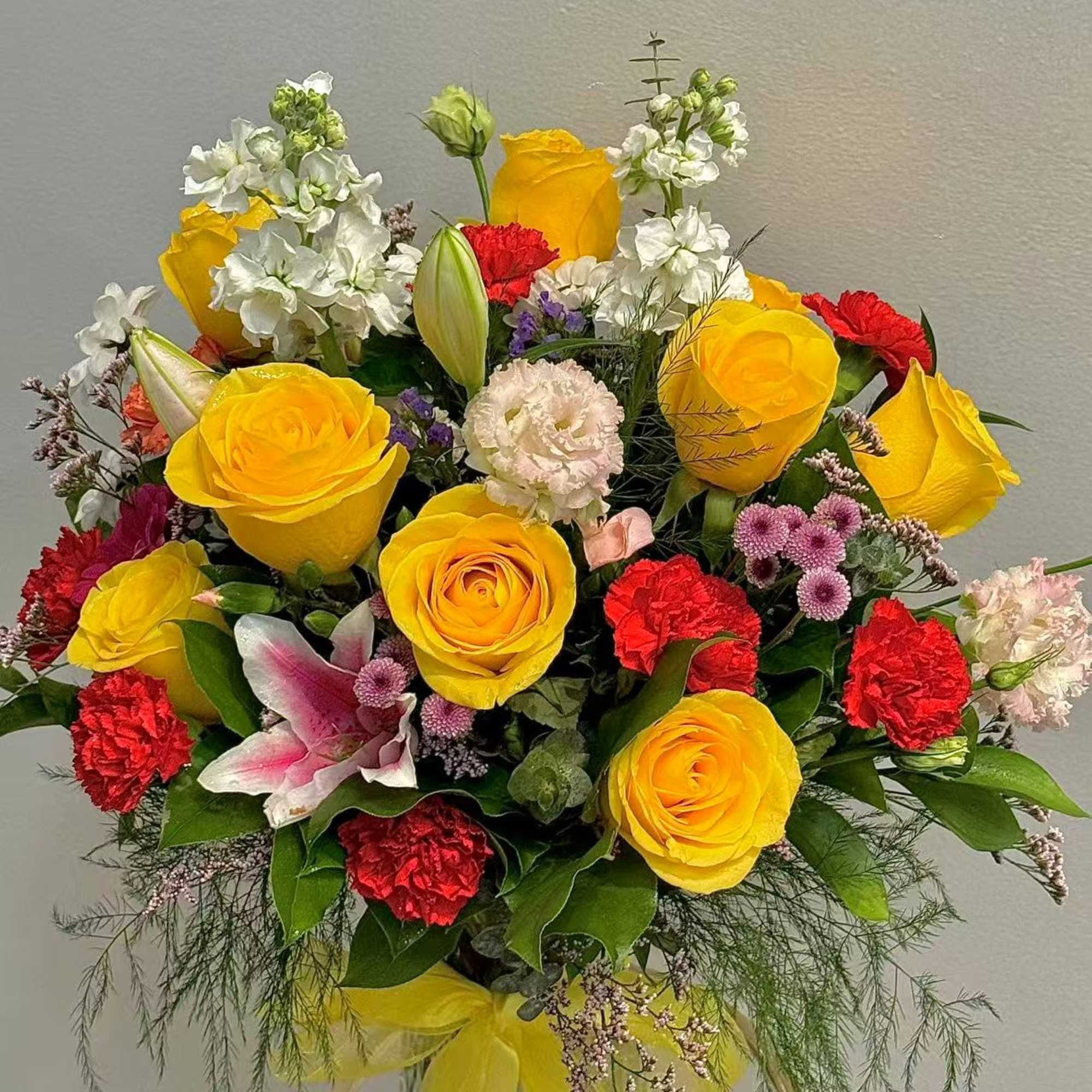 Bouquet of yellow roses, red carnations, and white flowers in a clear vase