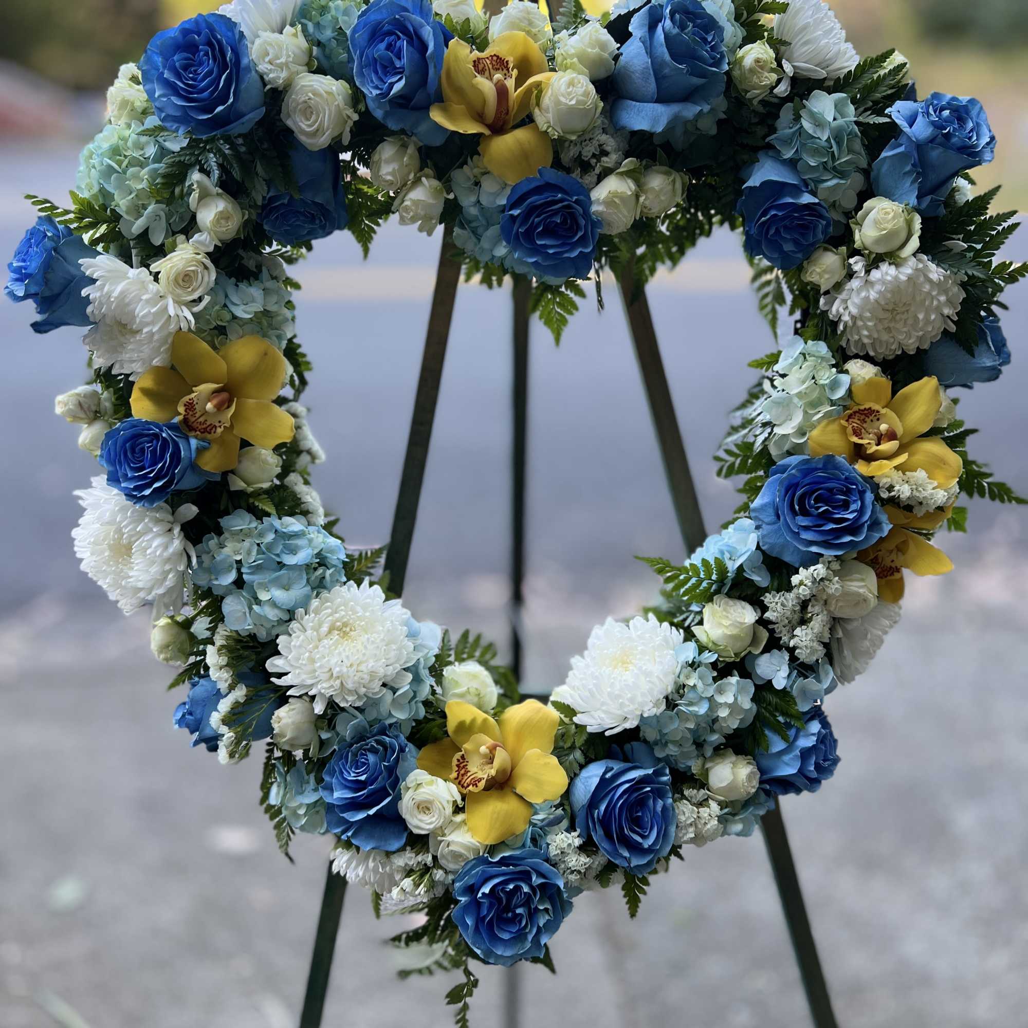 funeral wreath with blue roses, hydrangeas,  spray rose, and cymbidium orchids