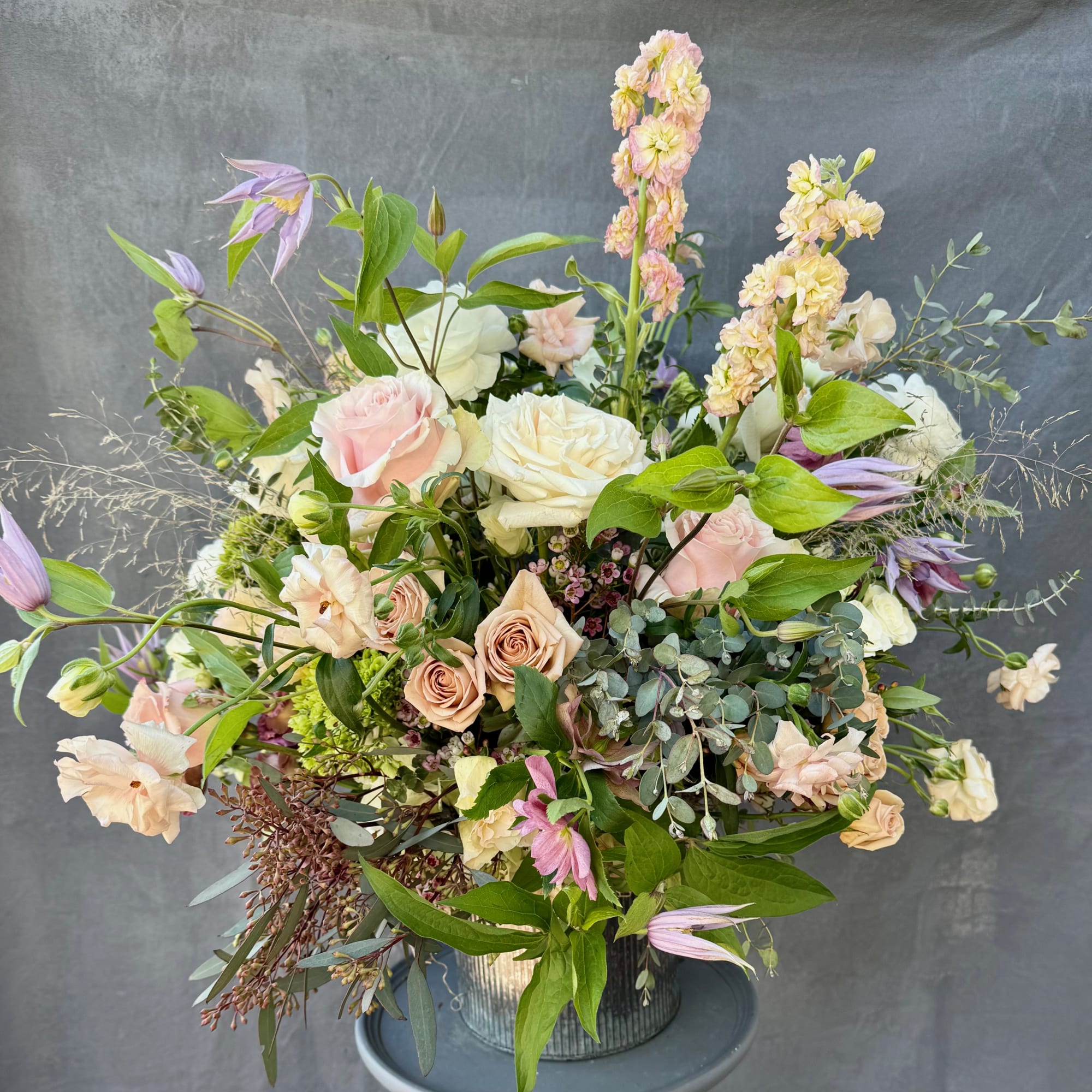 Loose bouquet of pale roses, lavender blooms, and greenery in a metal vase