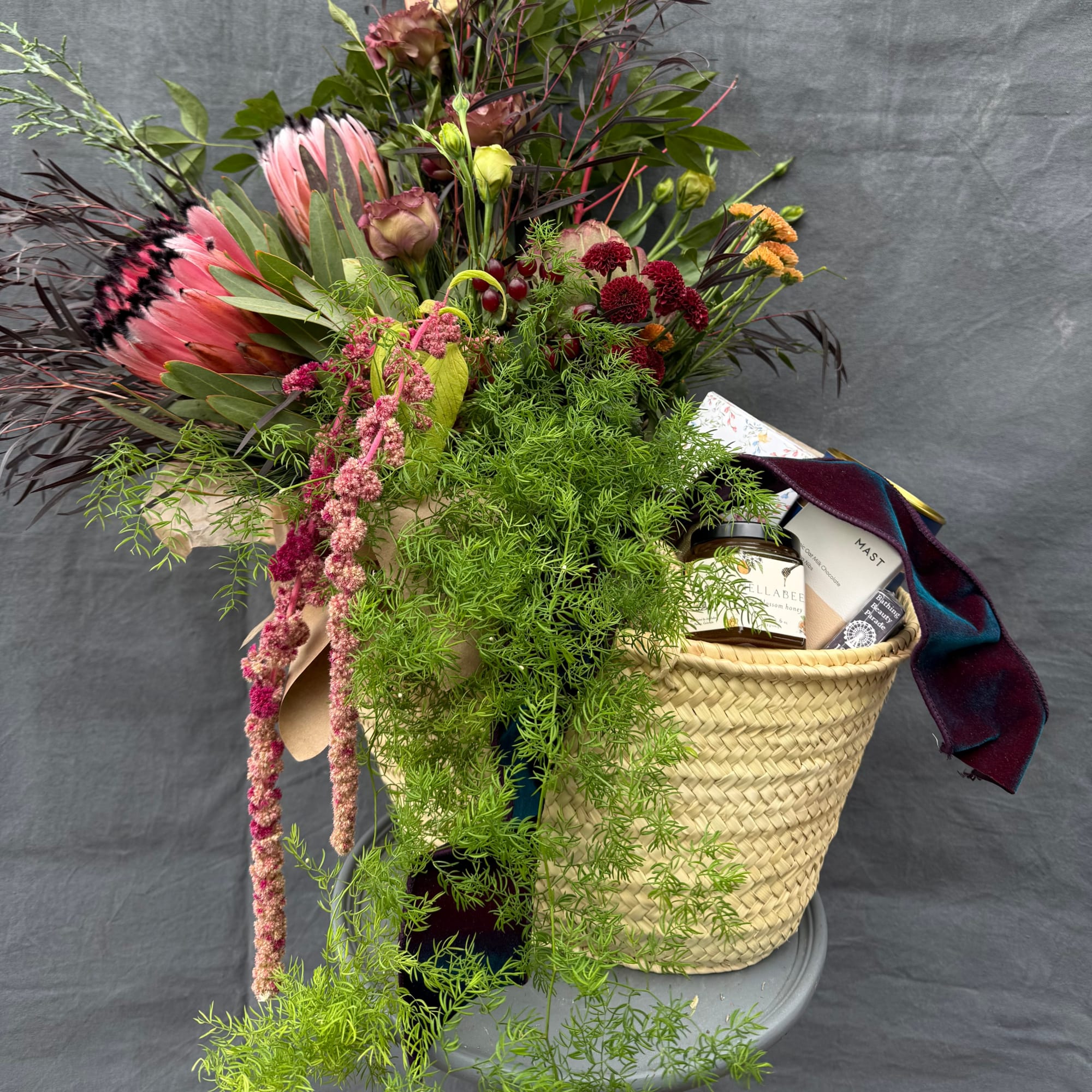 Mixed bouquet in a woven basket with a ribbon and gift items