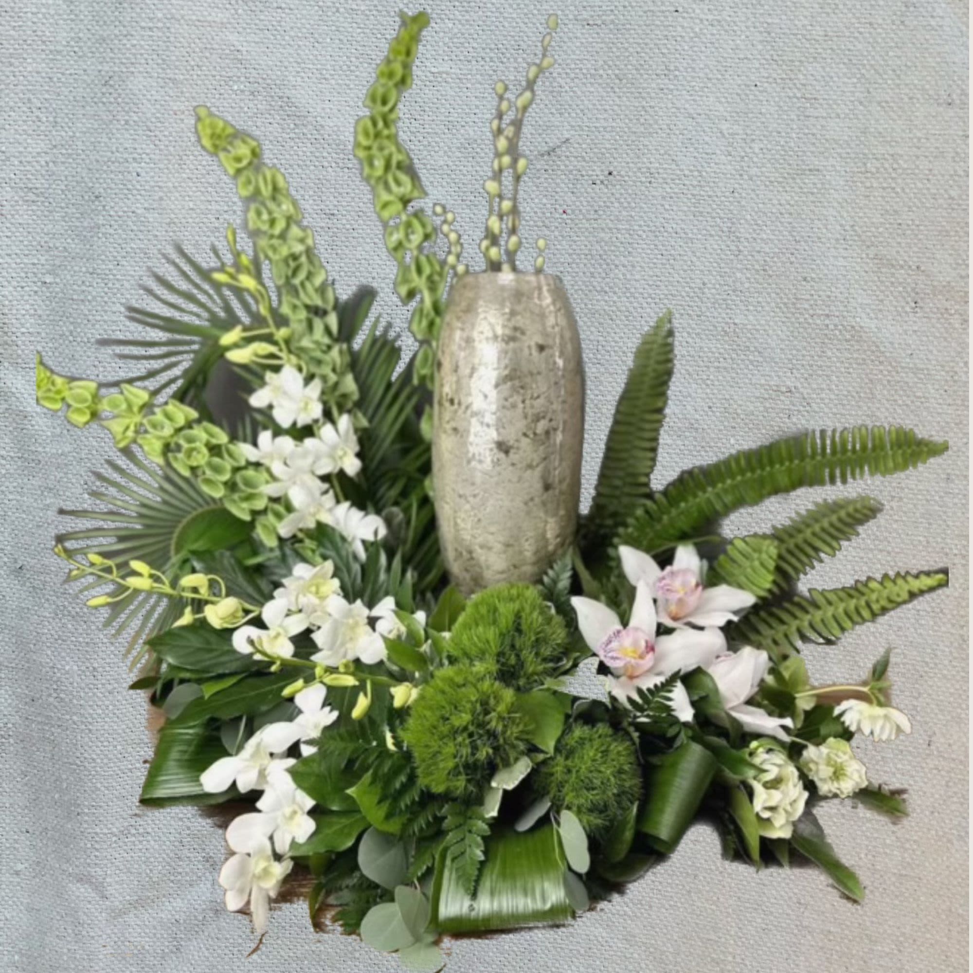 White orchids and green tropical foliage arranged around a tall metallic vase.