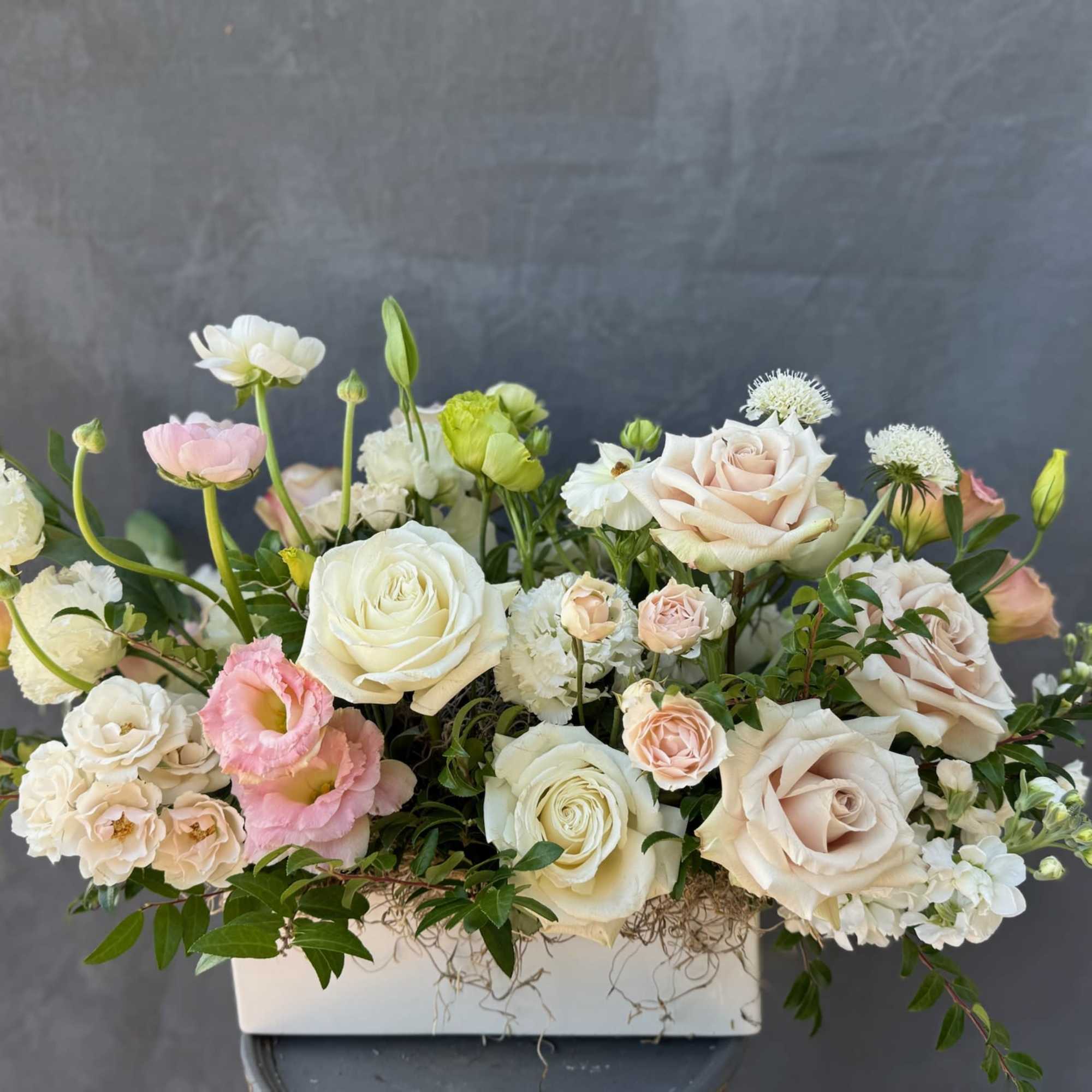 Pastel roses and mixed blooms arranged in a white rectangular vase