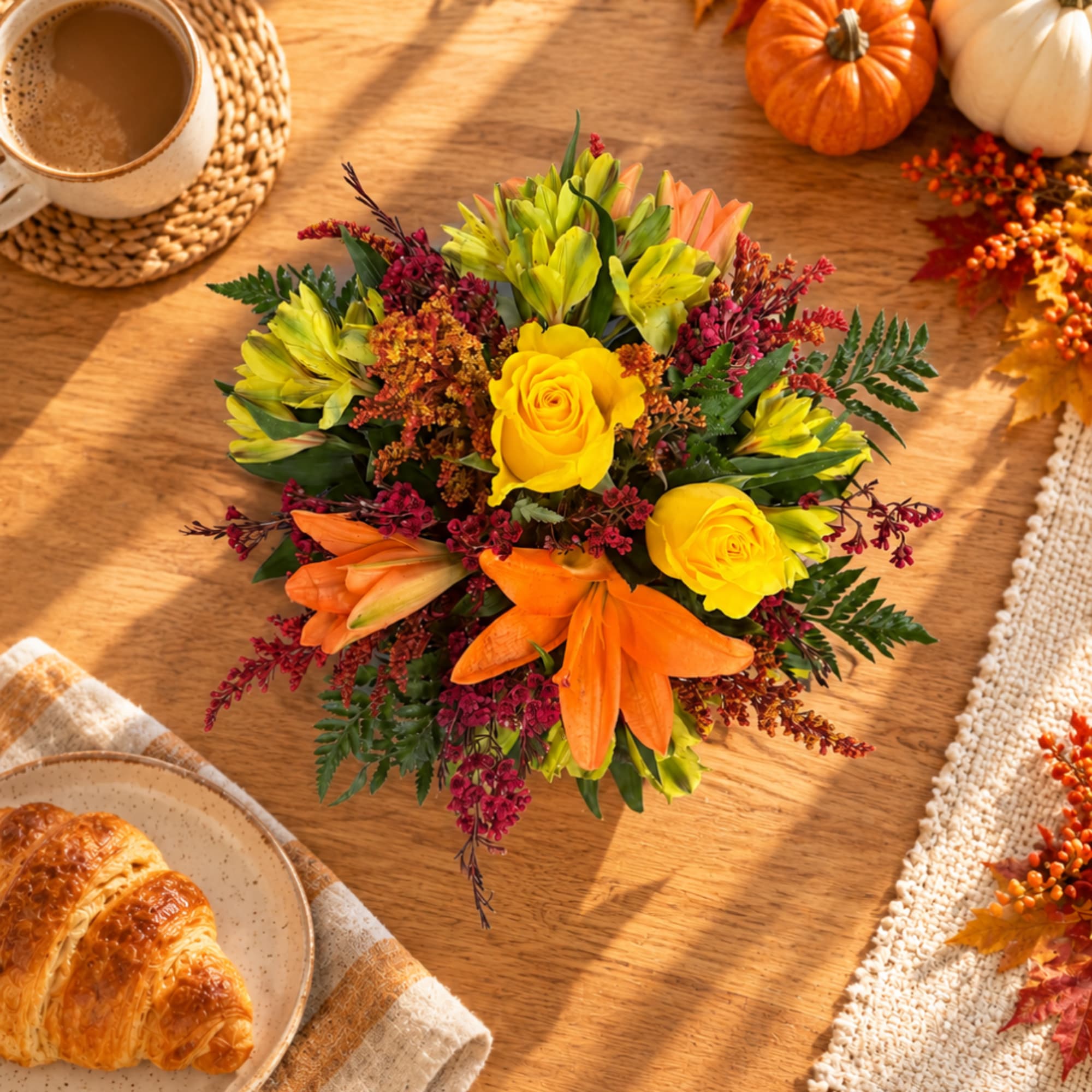 Autumn bouquet with yellow roses, orange lilies, and mixed greenery on a table