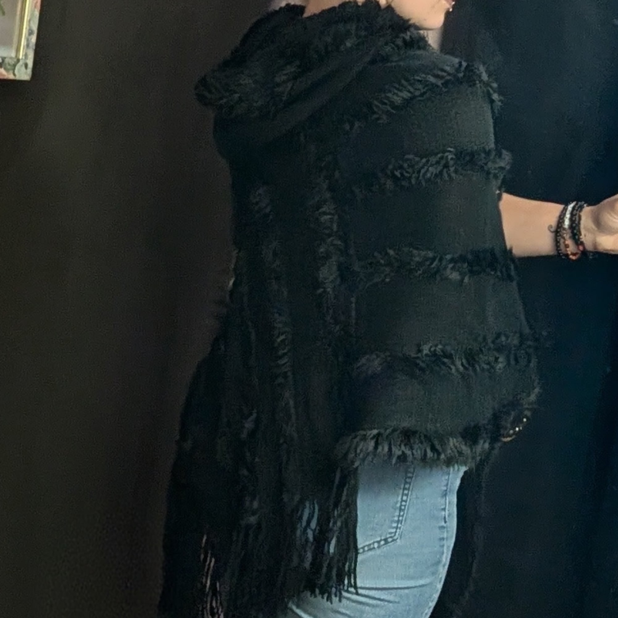 Person wearing a black fuzzy sleeveless top and light jeans