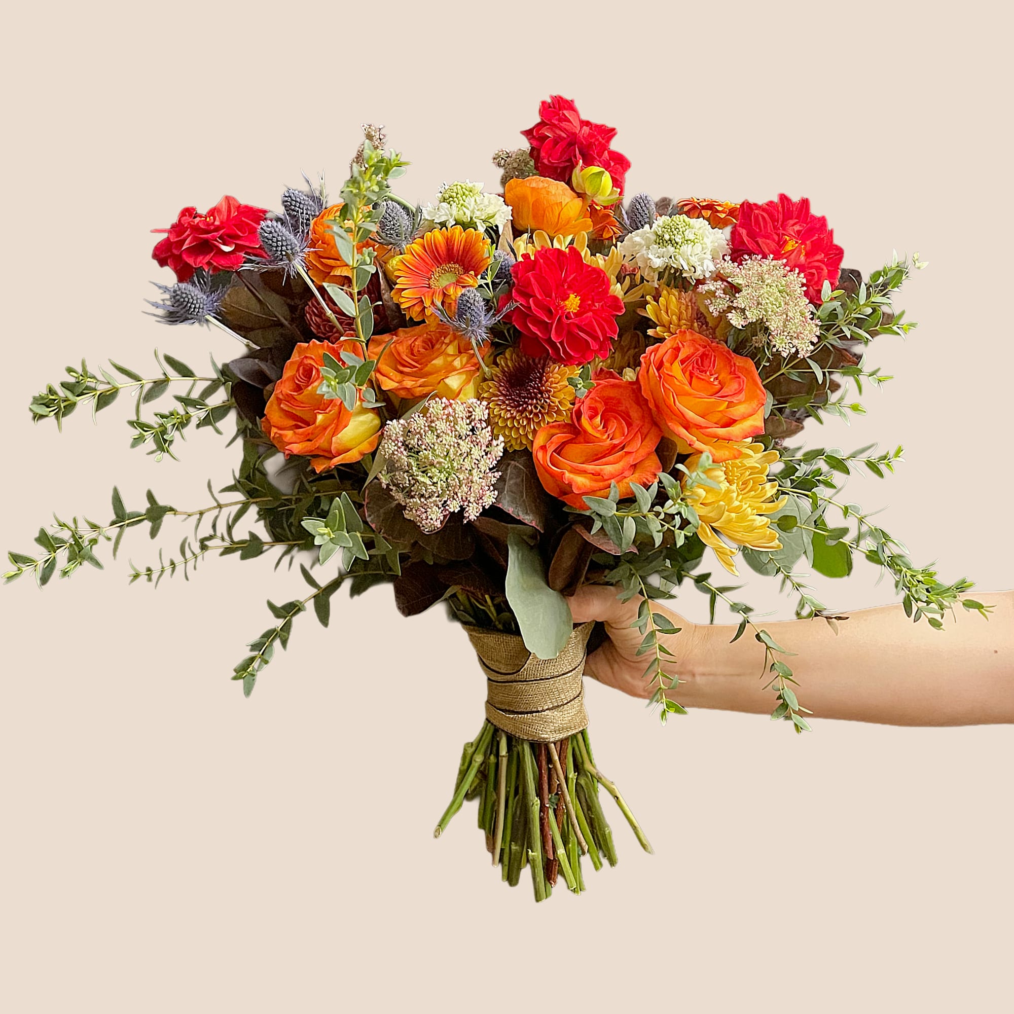 Handheld bouquet of orange and red flowers with greenery