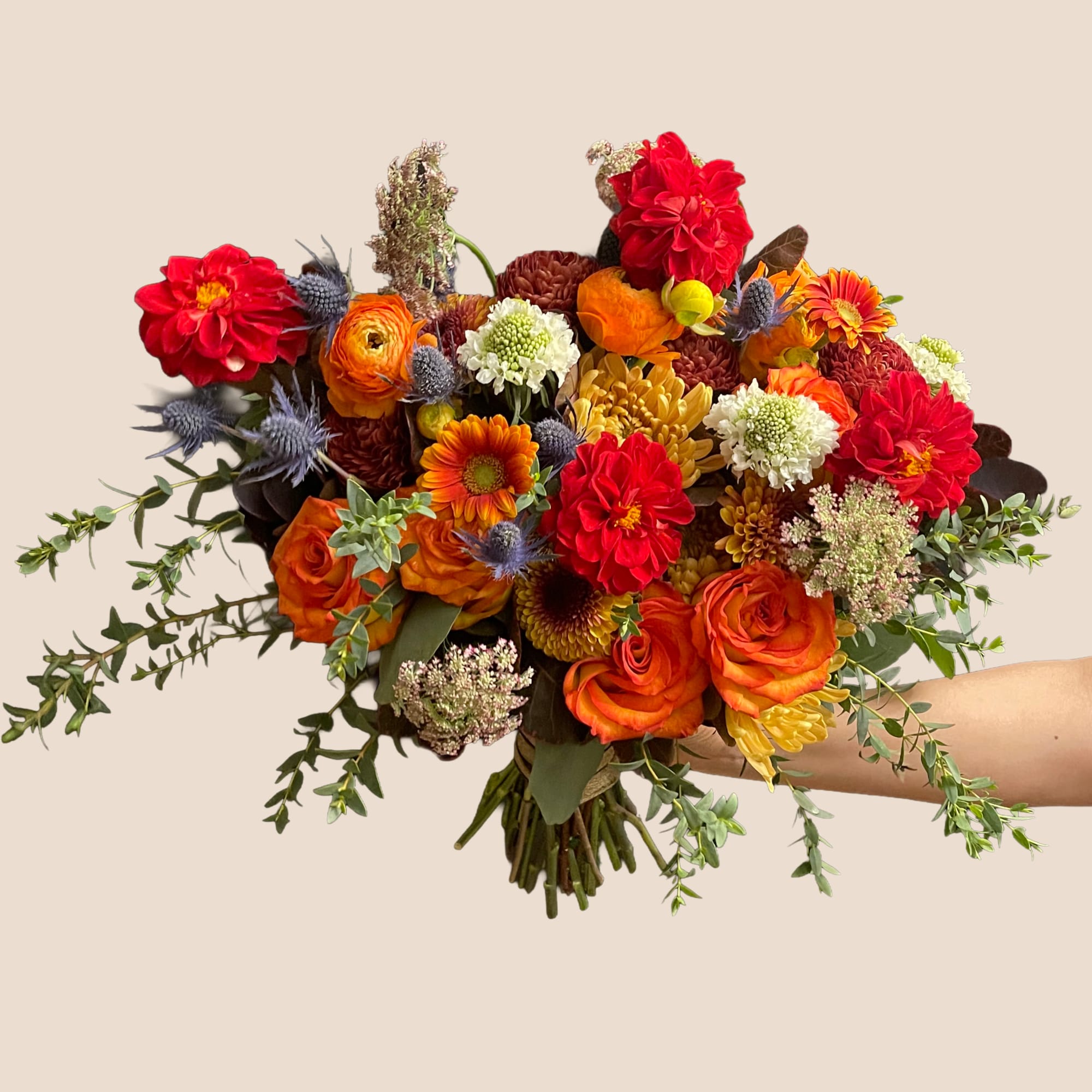 Handheld bouquet of red, orange, and yellow flowers with trailing greenery