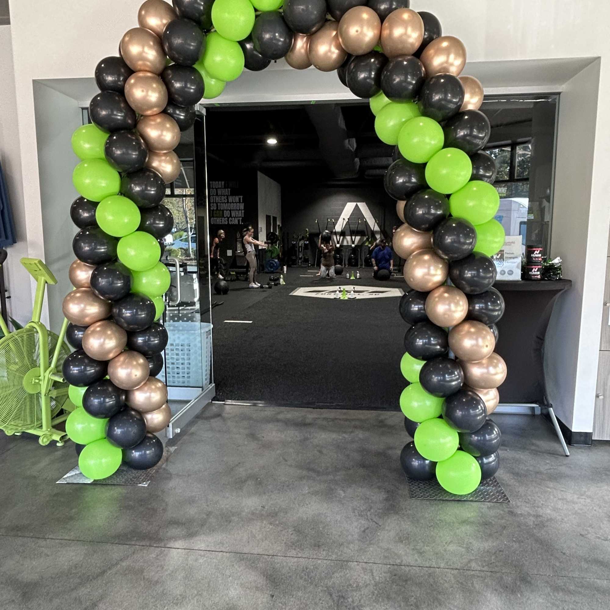 Balloon arch in neon green, black, and metallic gold at a gym entrance.
