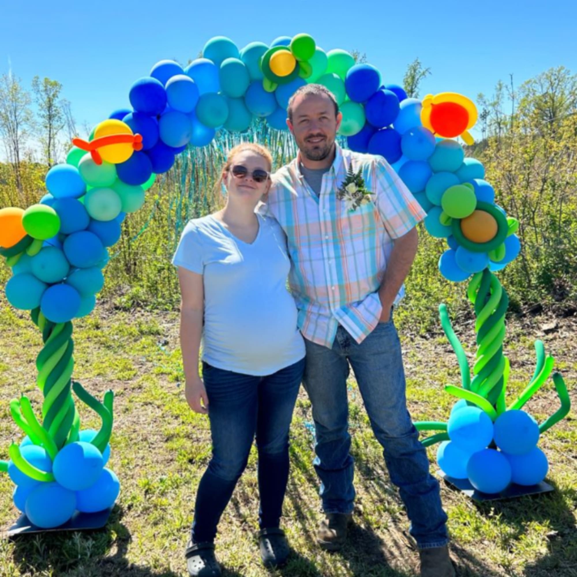 Two people standing under a colorful balloon arch outdoors