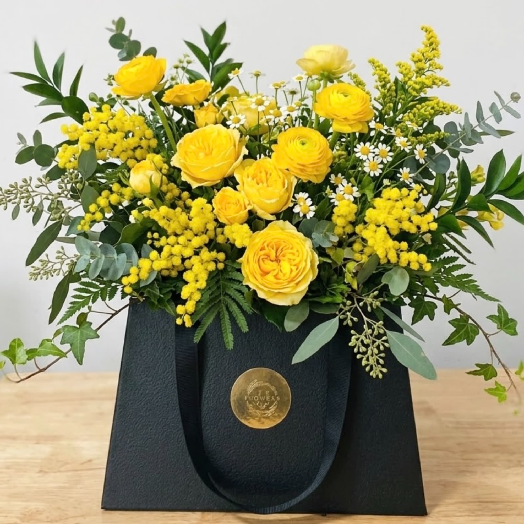 Yellow roses and mimosa in a black gift bag
