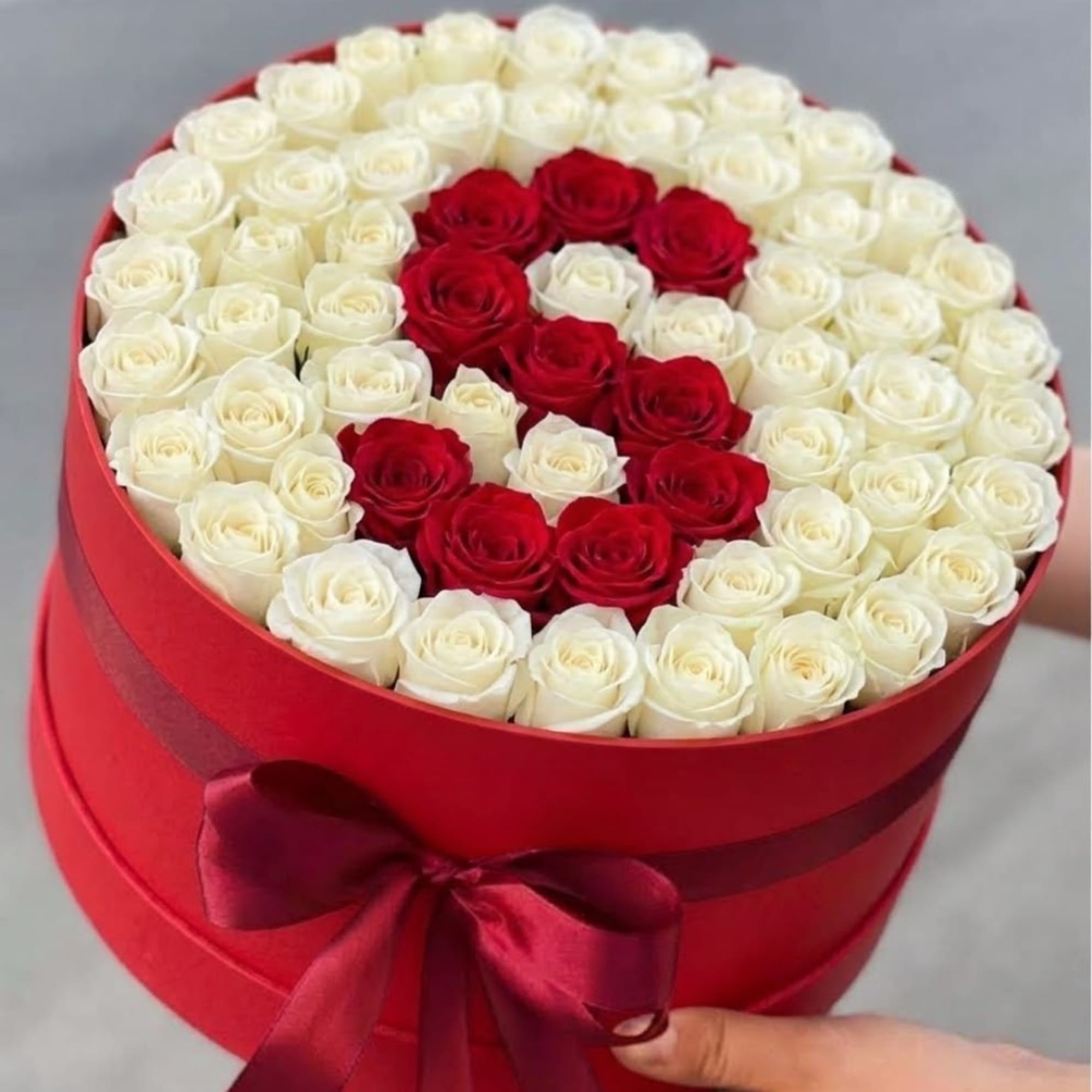 Red and white roses arranged in a round red box with a ribbon