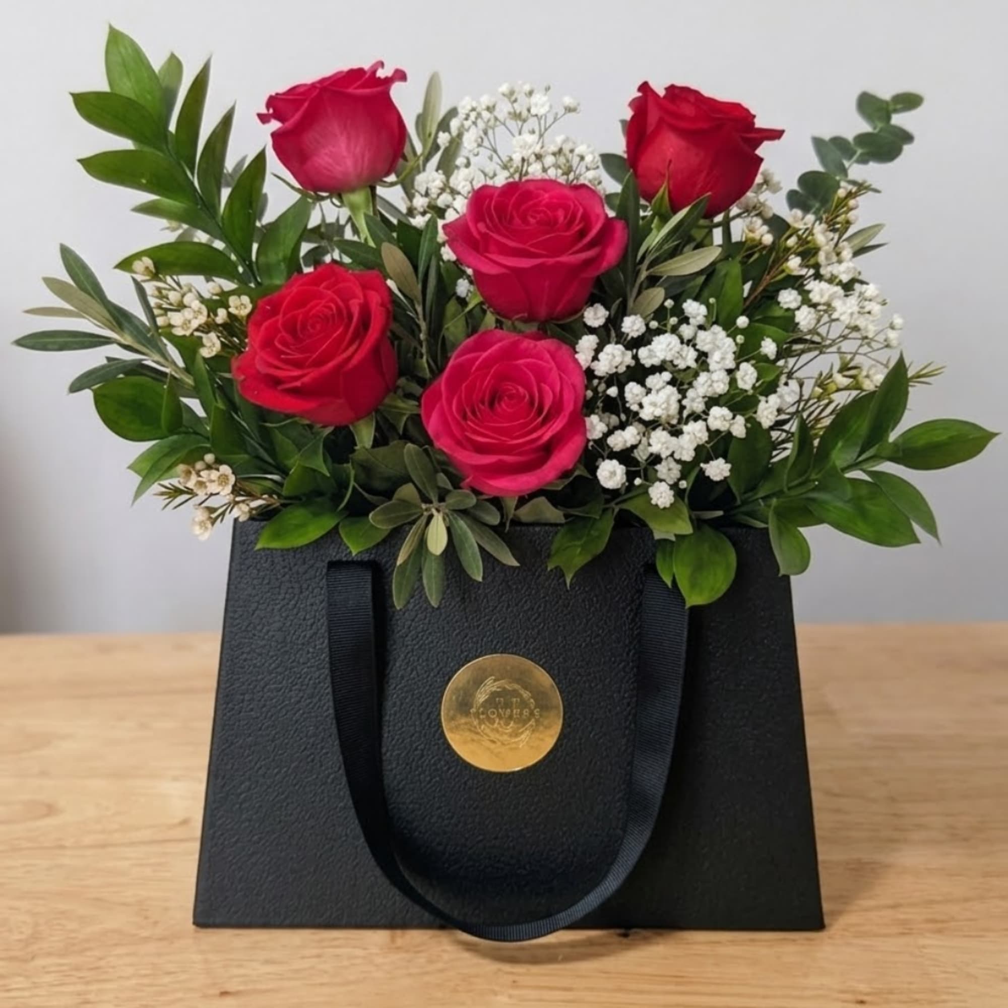 Red roses arranged in a black gift bag with white filler flowers