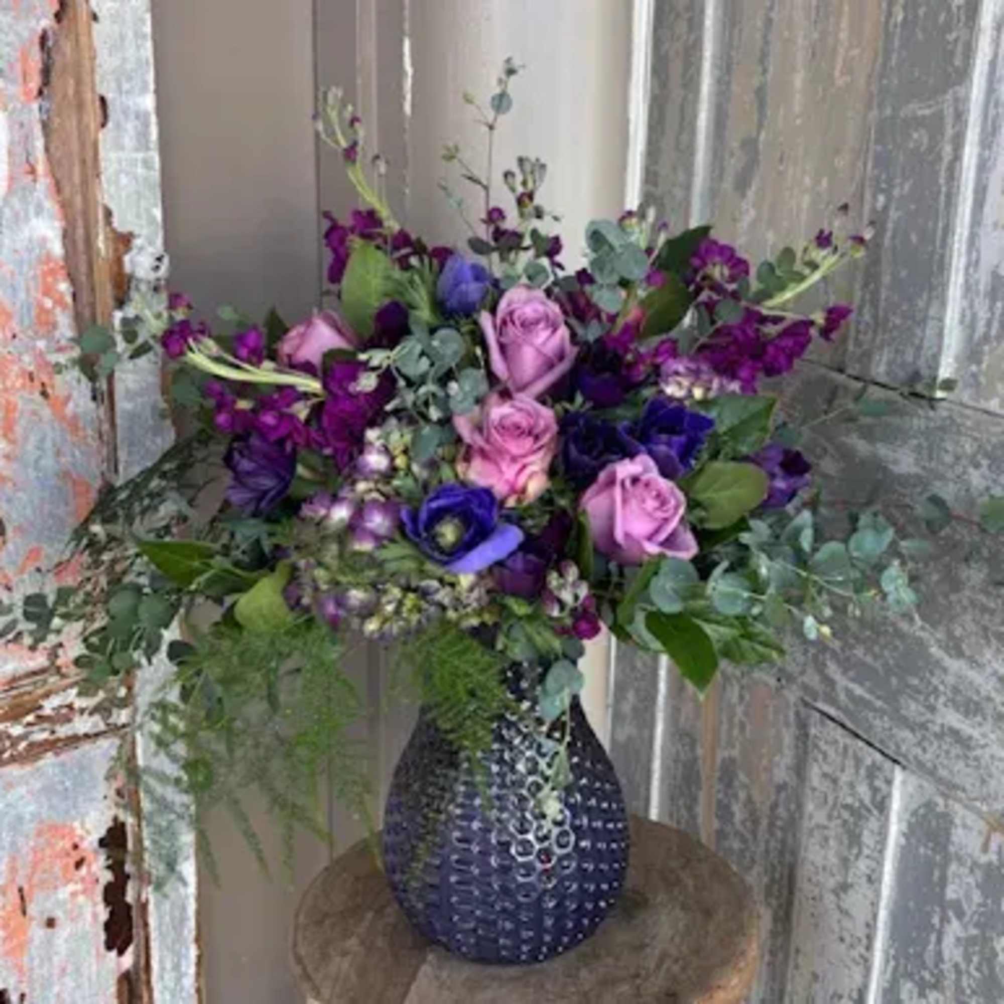Purple anemones, stock, hydrangea, and roses arranged with mixed greens and presented